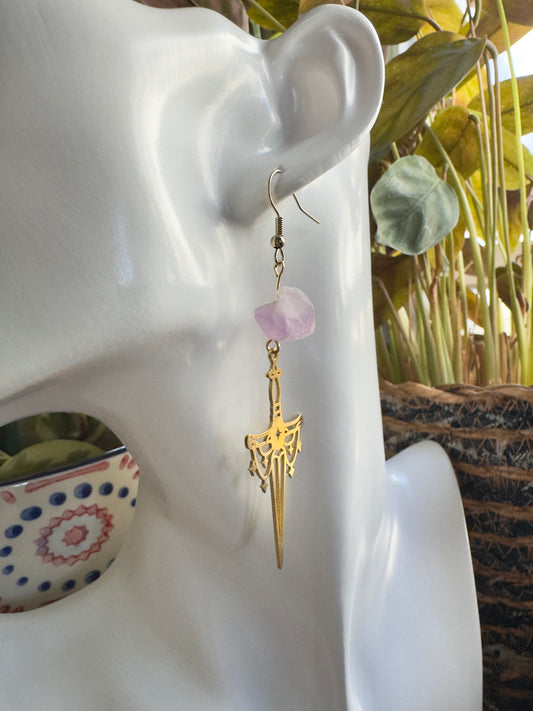 Gold sword earrings with amethyst chunk beads on a mannequin ear against a blurred indoor background