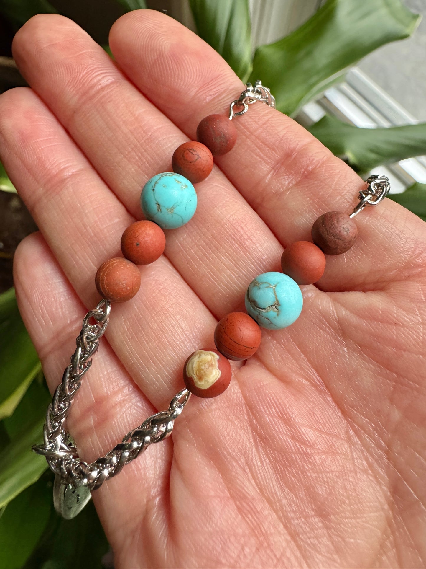 Bracelet with brown and turquoise beads on a hand, with a plant in the background
