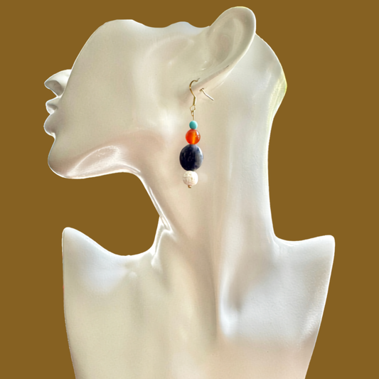 A single dangling beaded earring displayed on a glossy white female bust against a solid warm brown background. The earring features a gold fishhook clasp with stacked beads in turquoise, orange, dark navy blue, and white.