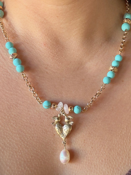 Close up of heart and birds pendant necklace on gold color chain with pearl, blue howlite and rose quartz beads