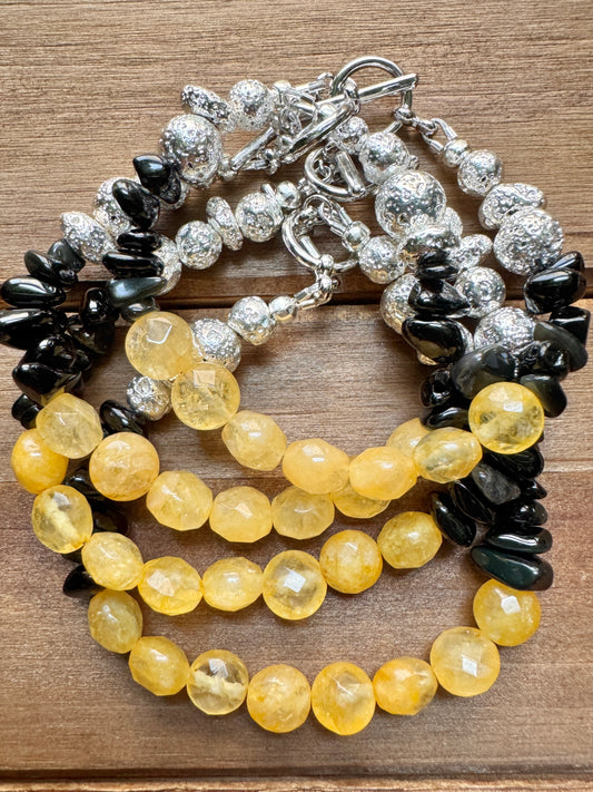 A multi-strand beaded bracelet featuring yellow faceted beads, black polished chips, and textured silver beads with a silver toggle clasp, displayed on a brown wooden surface.