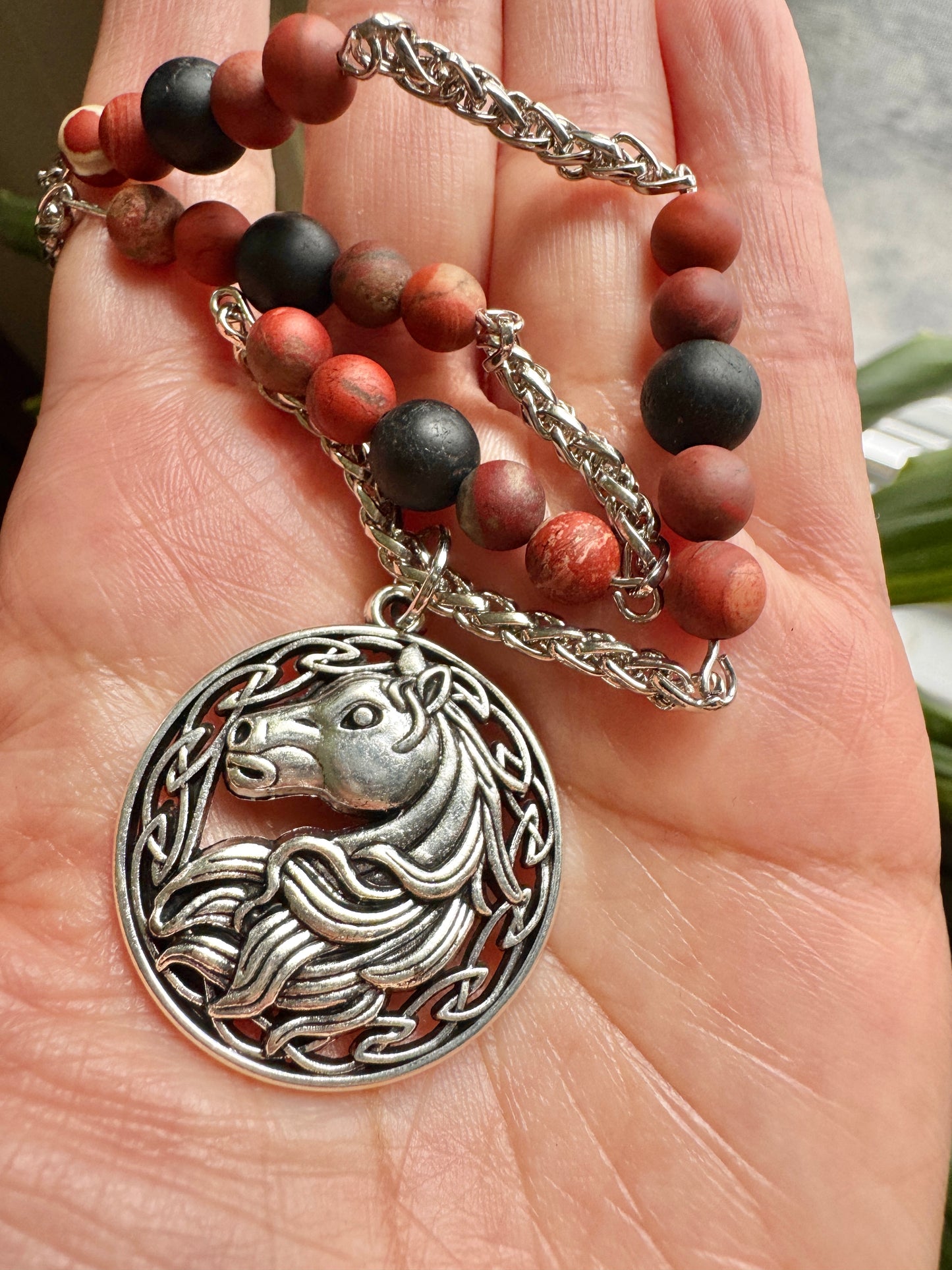 Hand holding a necklace with a horse pendant and beaded chain.