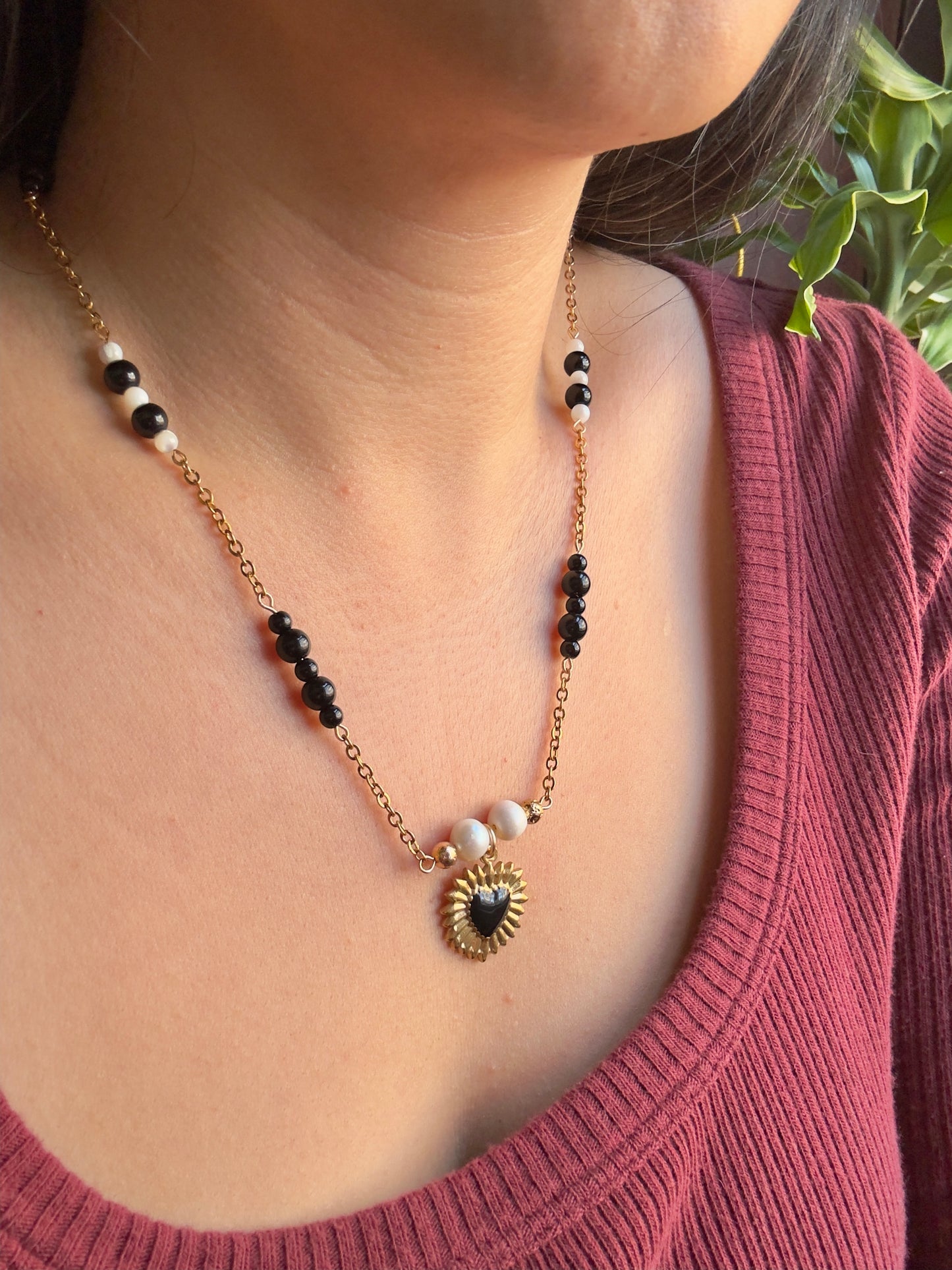 Black heart gold stainless steel pendant on gold stainless steel chain with black jasper and pearl beads, slight side view on model