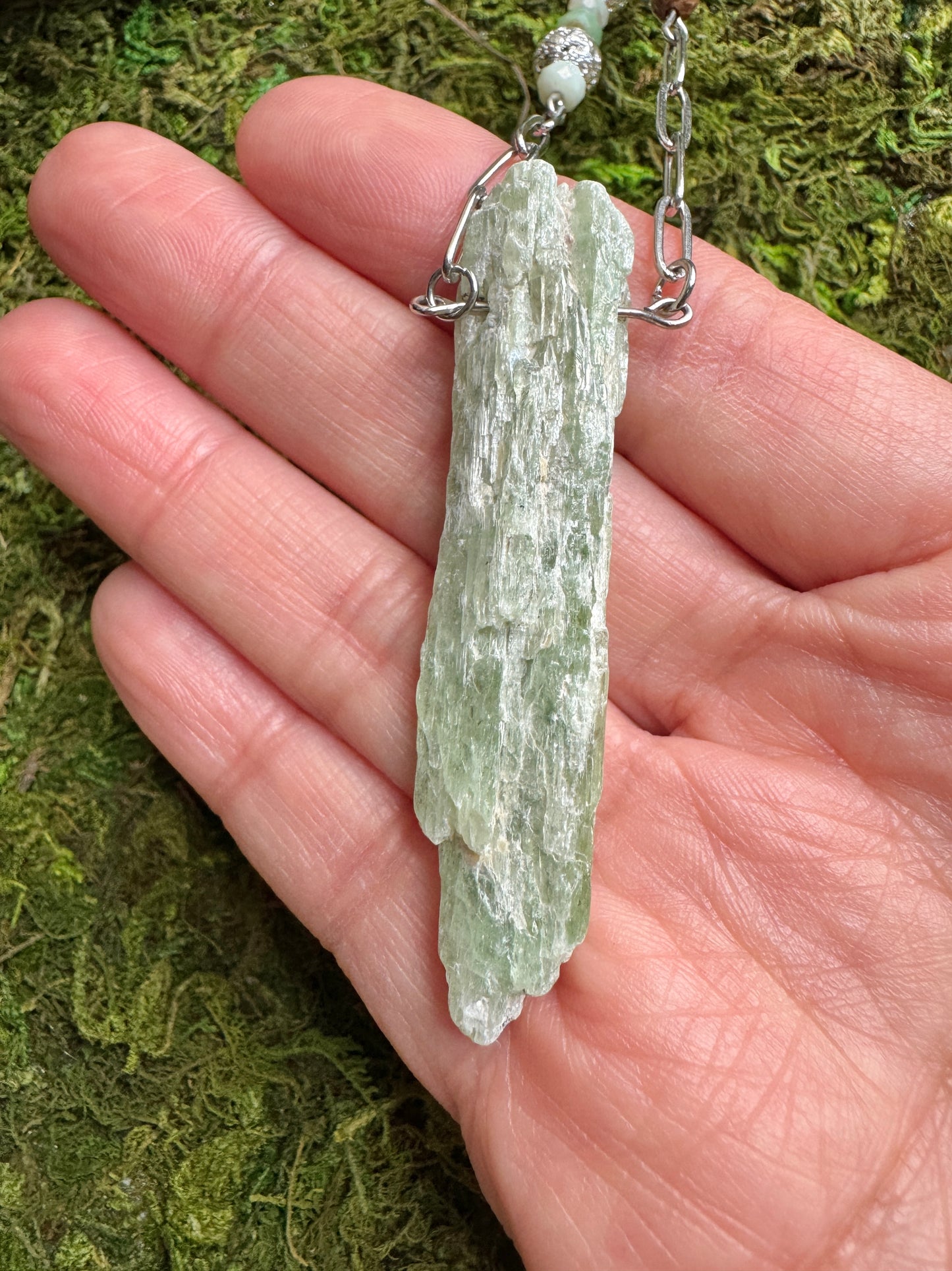 Crystal pendant on a chain held in a hand with a mossy background