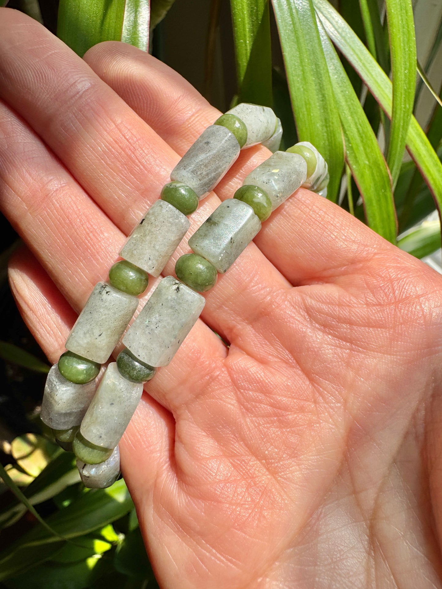 Hand holding a bracelet with green and gray beads against a natural background