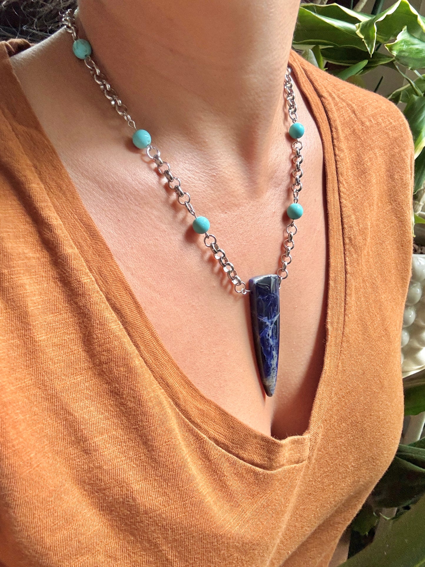 Necklace with turquoise beads and a large blue stone pendant on a person wearing a mustard yellow top.