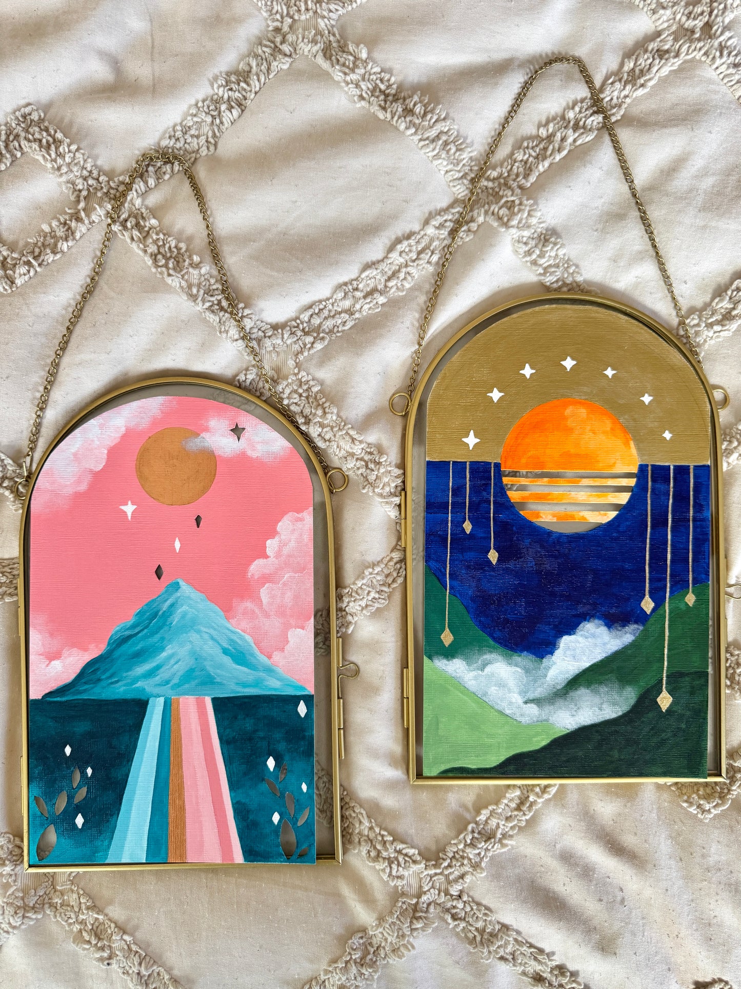 Two landscape paintings against arched glass frames resting on a white background
