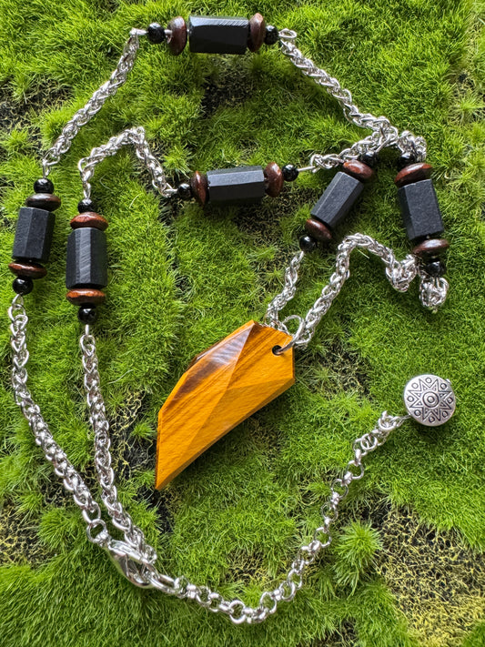 Necklace with wooden pendant and black beads on a green moss background