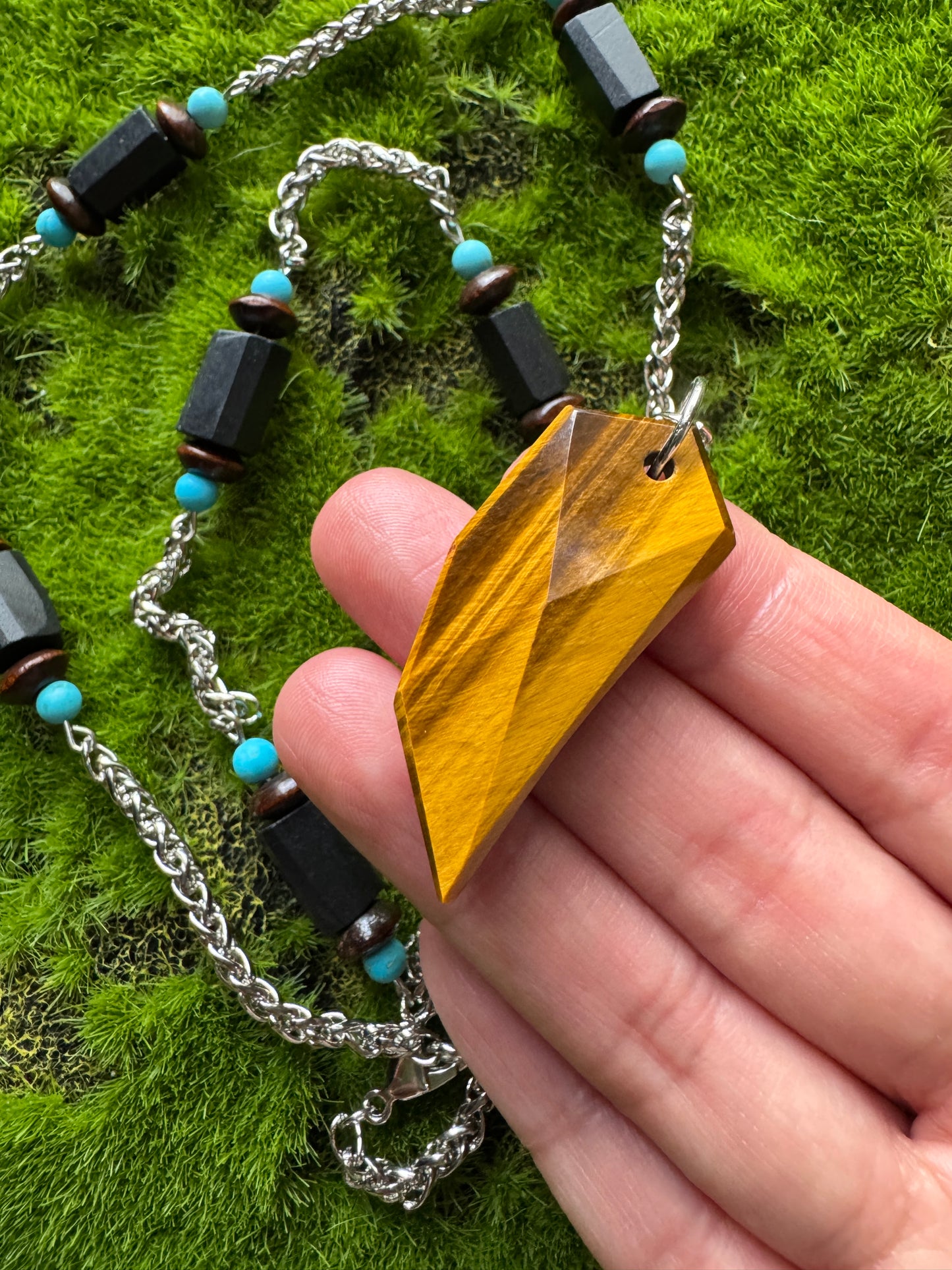 Hand holding a necklace with a yellow pendant on a green grass background