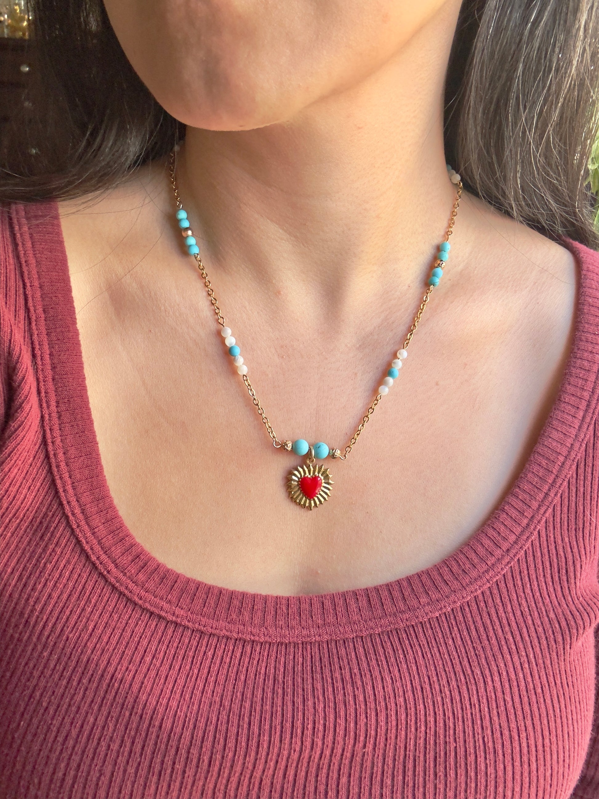 Red enamel gold stainless steel heart pendant on gold stainless steel chain with blue howlite and mother of pearl beads, close up on model