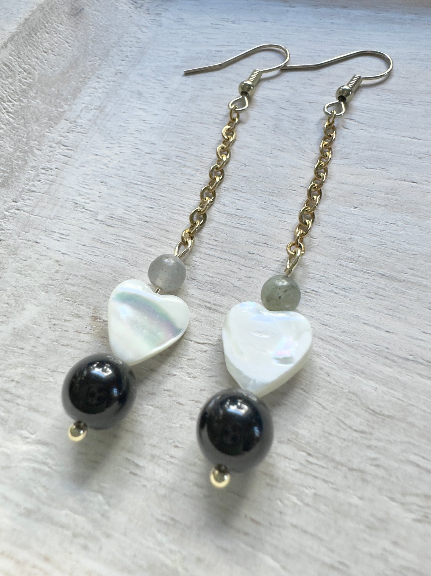Pair of earrings with heart-shaped and round beads on a light wooden surface
