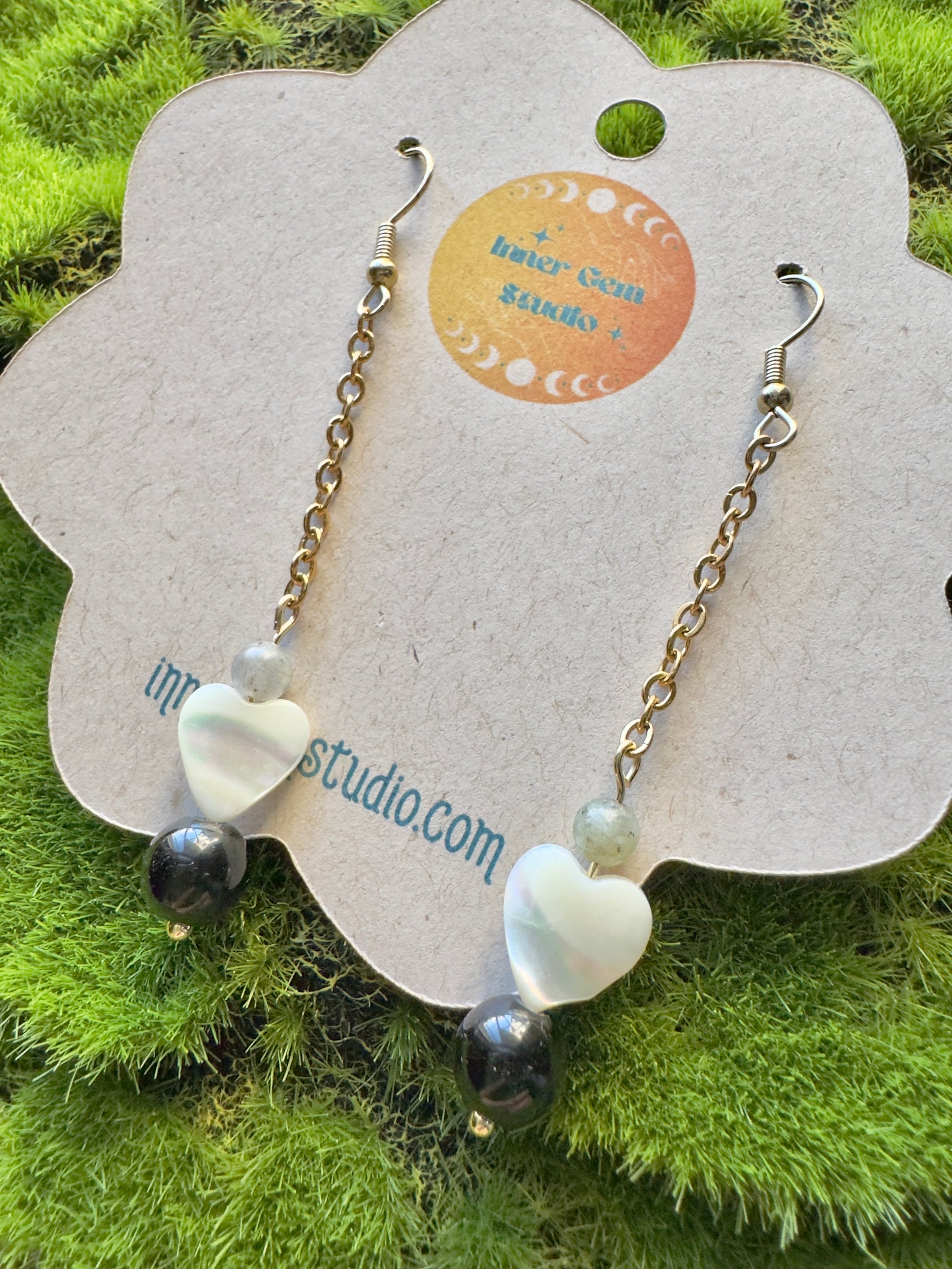 Pair of beaded earrings on a floral card with 'innergem studio.com' branding, set against a grassy background.