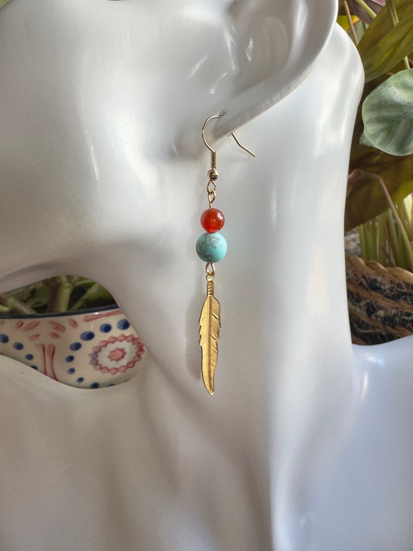 Earring with feather and bead design on a mannequin ear, close-up