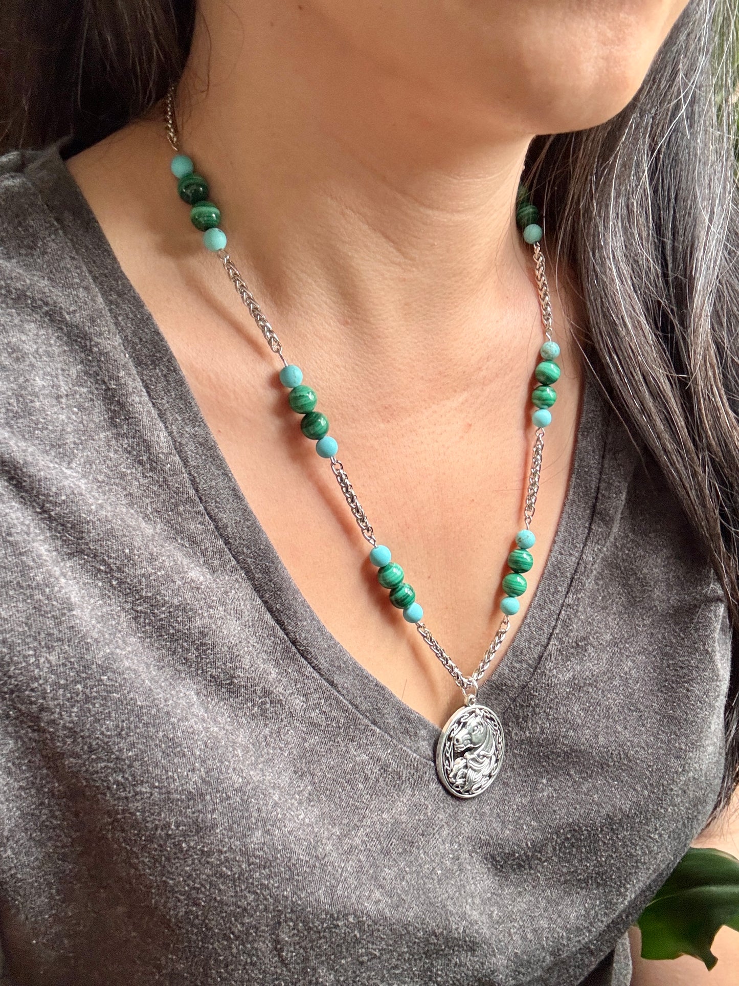 Necklace with green beads and a silver pendant worn by a person in a gray shirt.