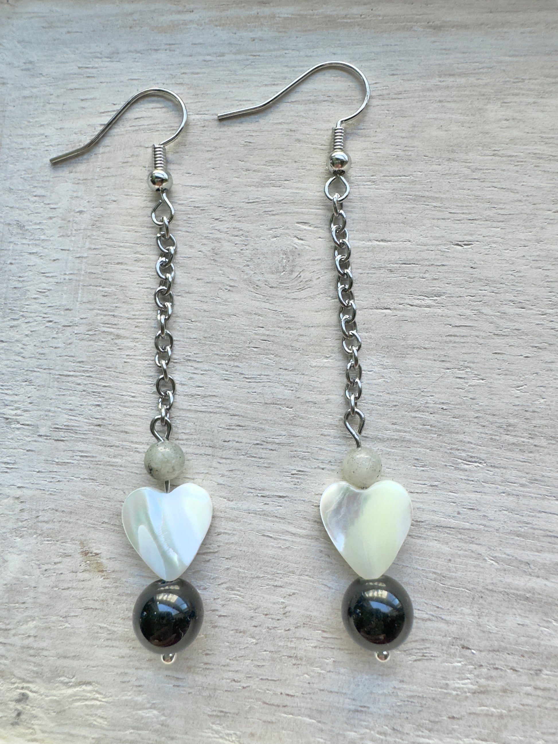 Pair of earrings with heart-shaped beads and black stones on a light wooden surface