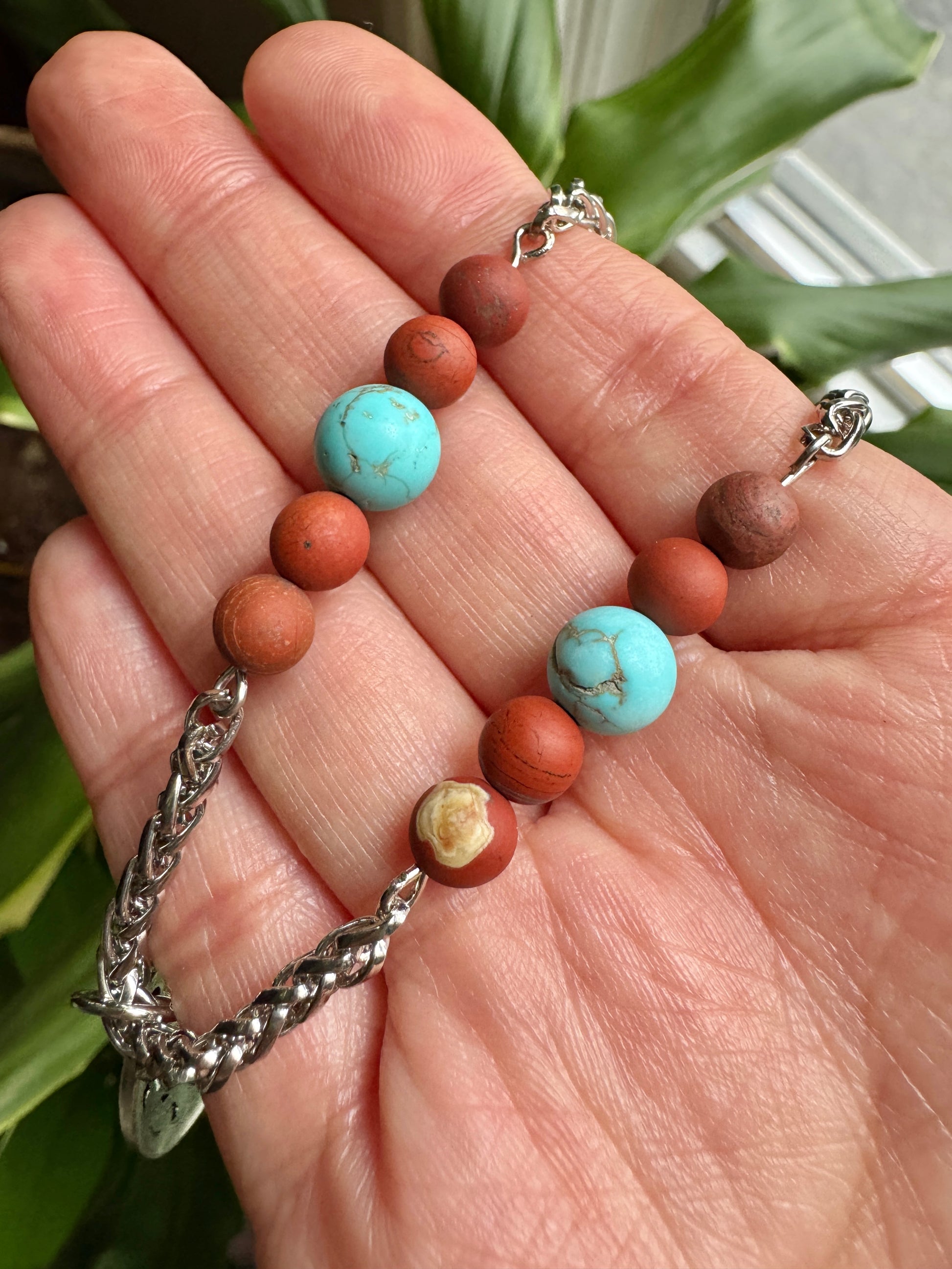 Bracelet with brown and turquoise beads on a hand, with a plant in the background
