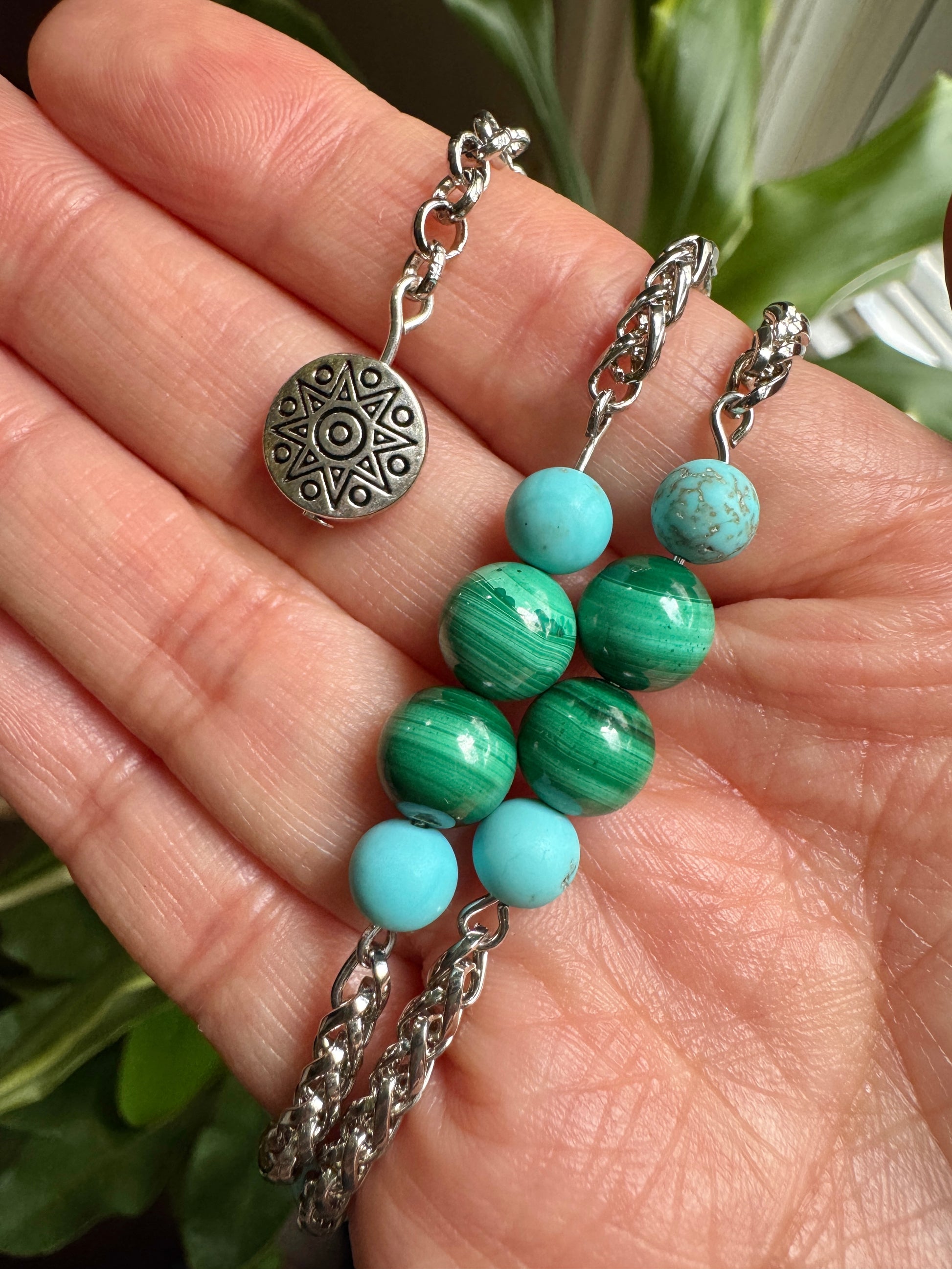 Turquoise beaded earrings with silver chains held in a hand against a green leafy background