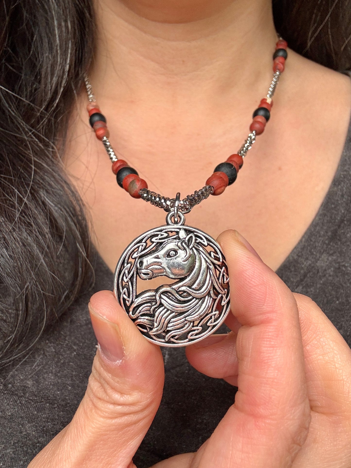 Person holding a silver necklace with a horse pendant