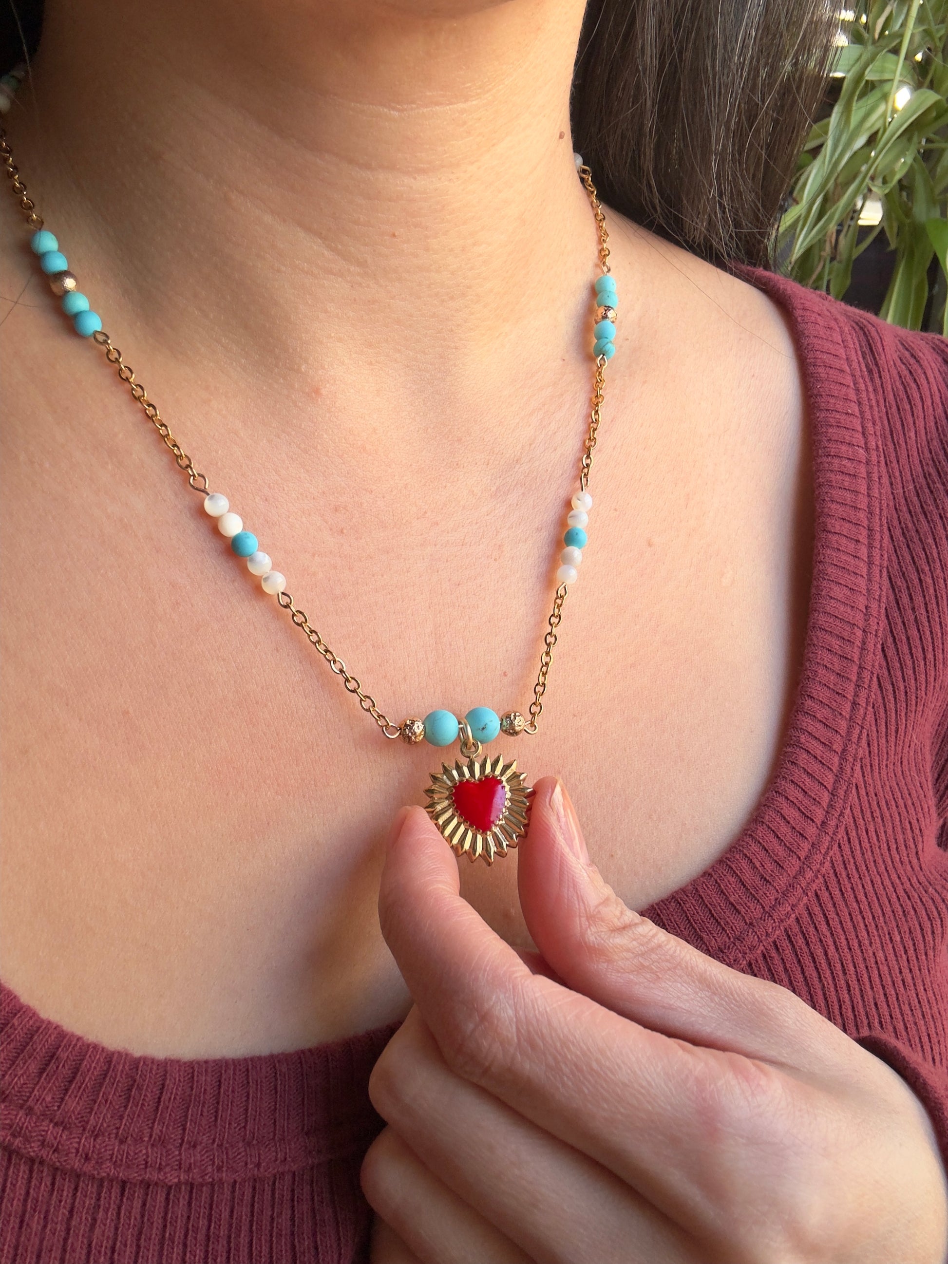 Red enamel gold stainless steel heart pendant on gold stainless steel chain with blue howlite and mother of pearl beads, with model holding out heart pendant