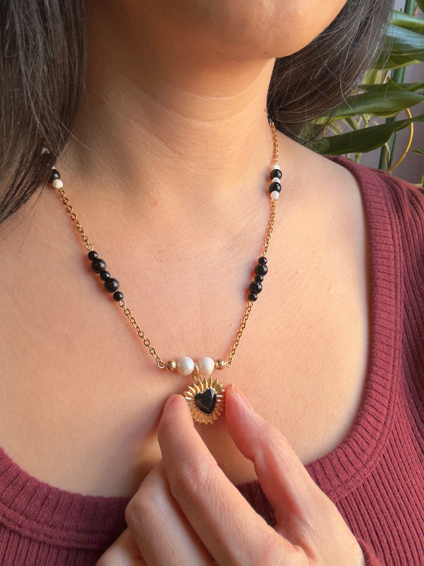 Black heart gold stainless steel pendant on gold stainless steel chain with black jasper and pearl beads, model holds up heart pendant 