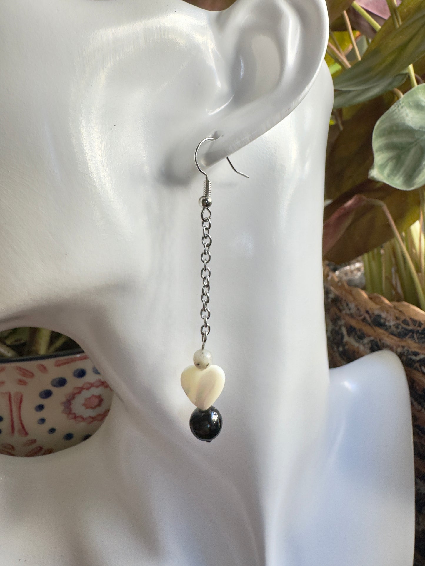 Earring with a heart-shaped pearl and black bead on a mannequin ear.