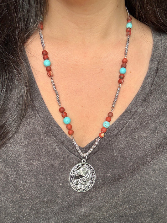 Necklace with a horse pendant and beaded chain worn by a person on a gray shirt