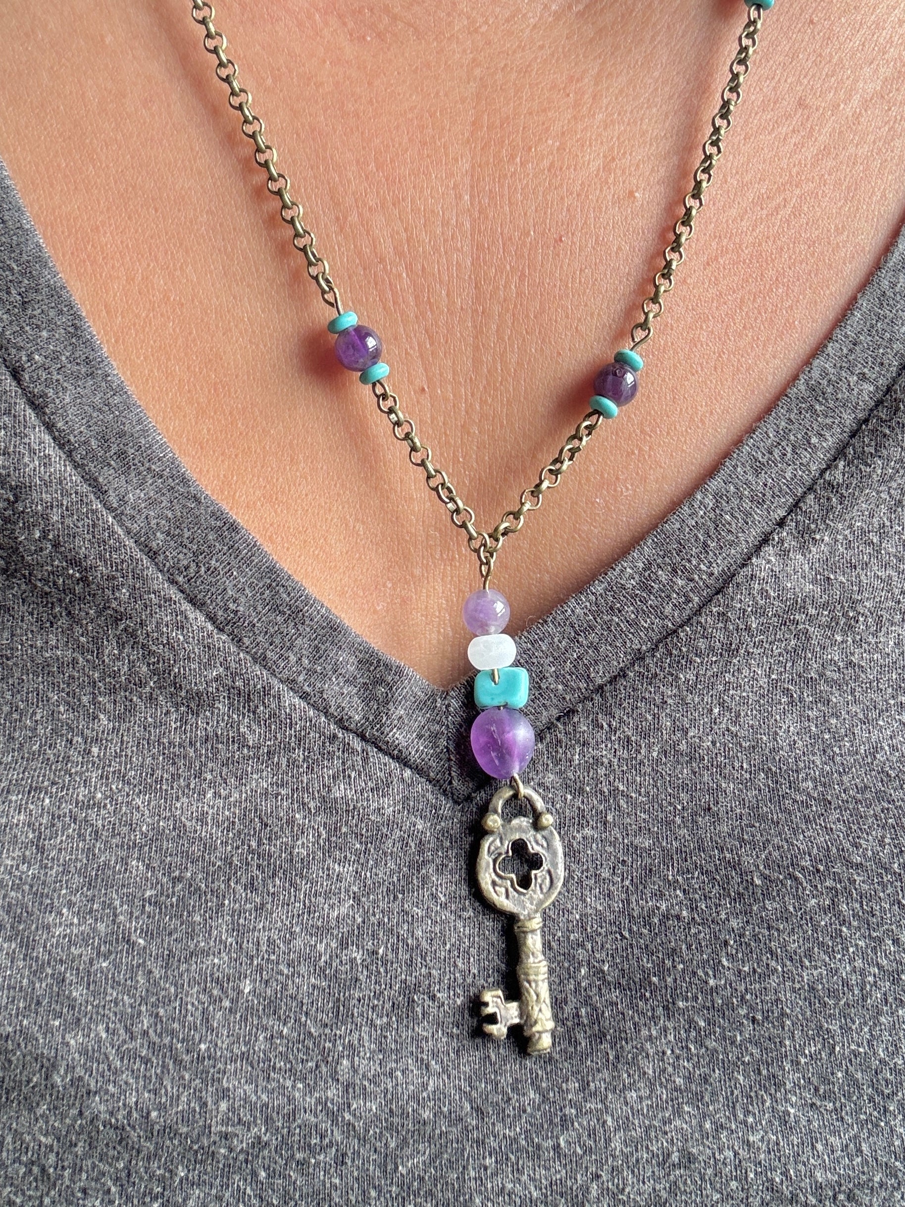 Necklace with a key pendant and colorful beads worn by a person in a gray shirt.