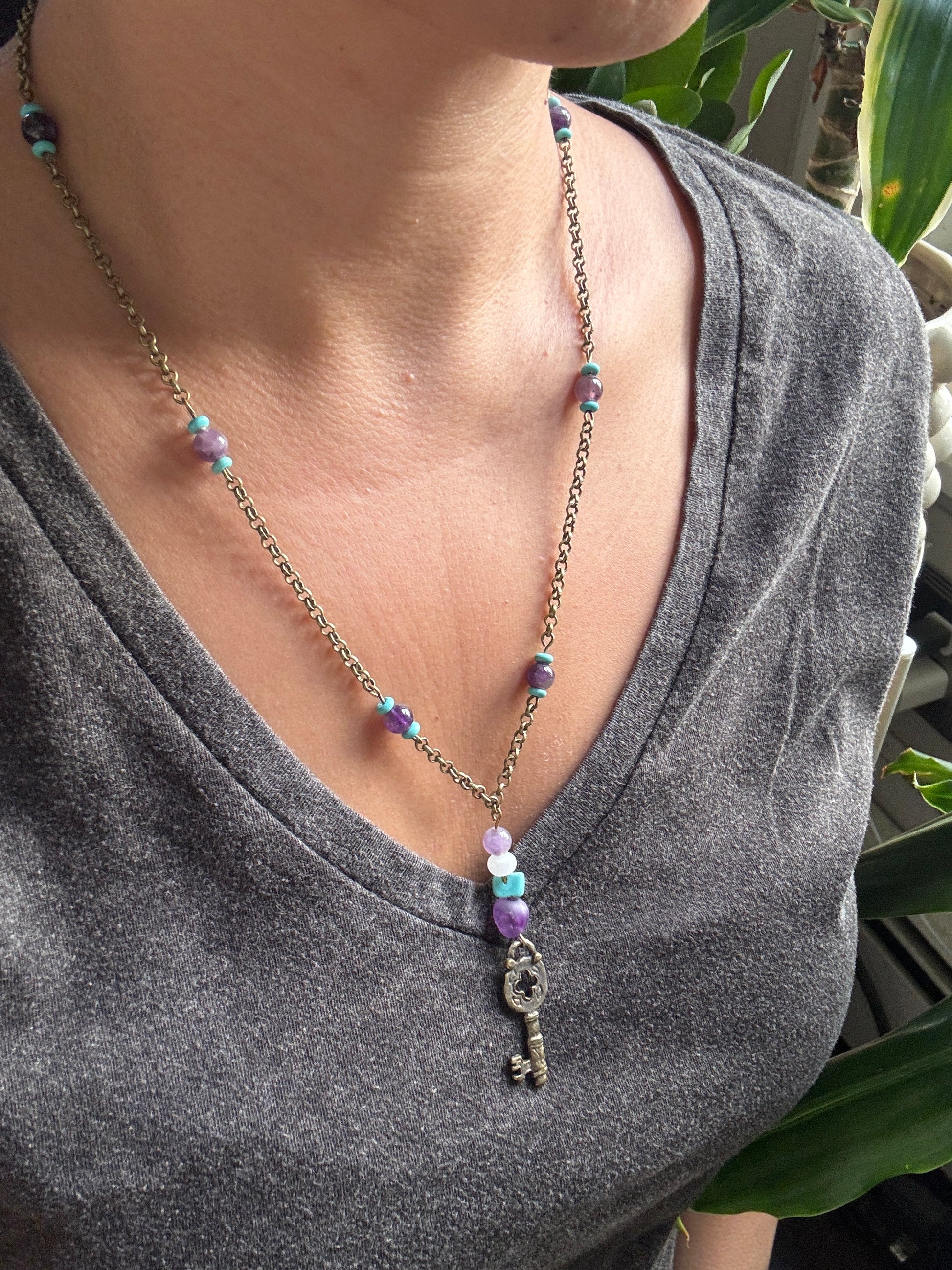 Necklace with a key pendant and beaded chain worn by a person, with a blurred background.