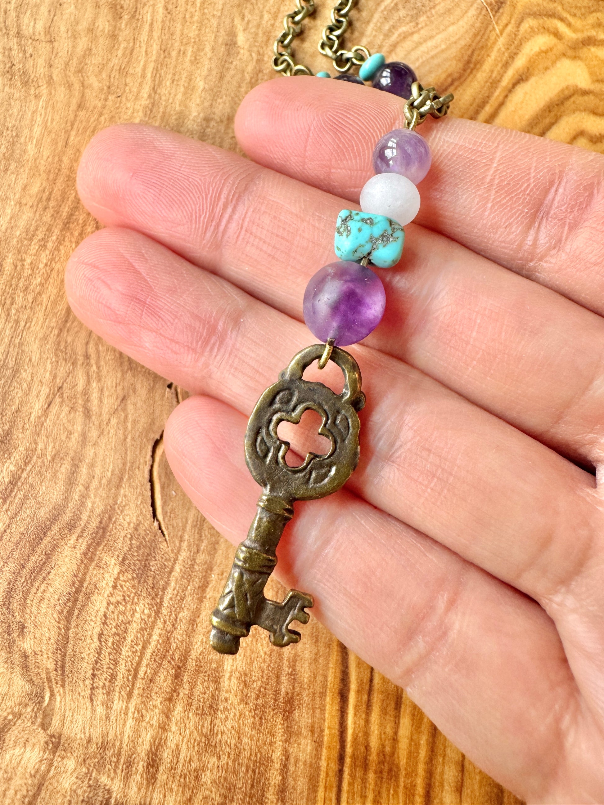 Necklace with a vintage-style key pendant and colorful beads held by a hand on a wooden surface