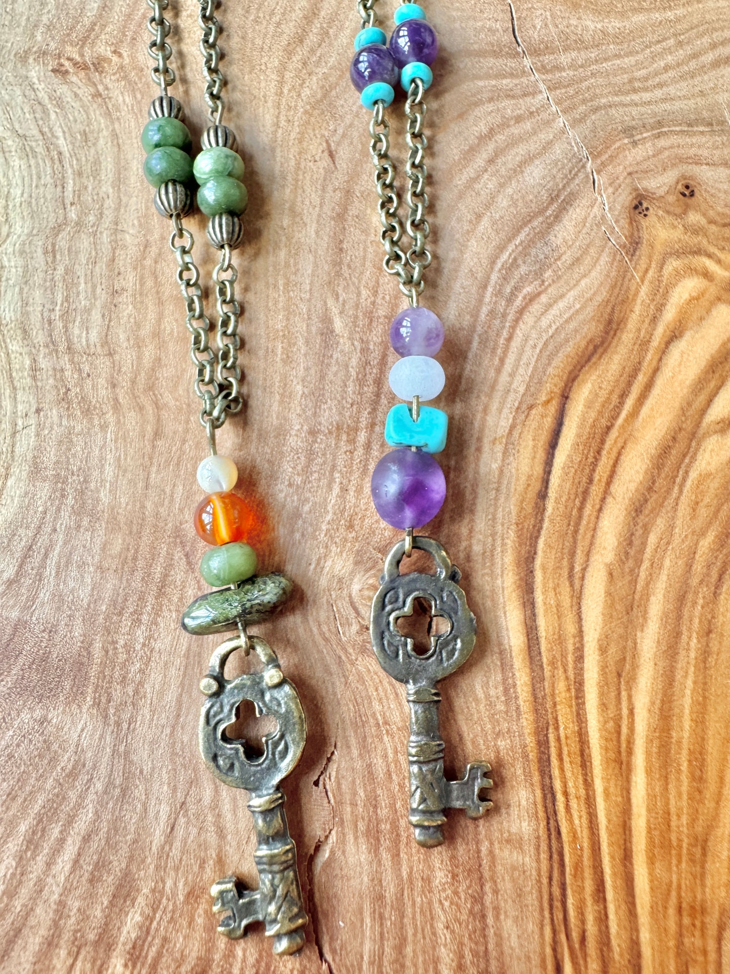 Two key-shaped pendants on chains with colorful beads against a wooden background