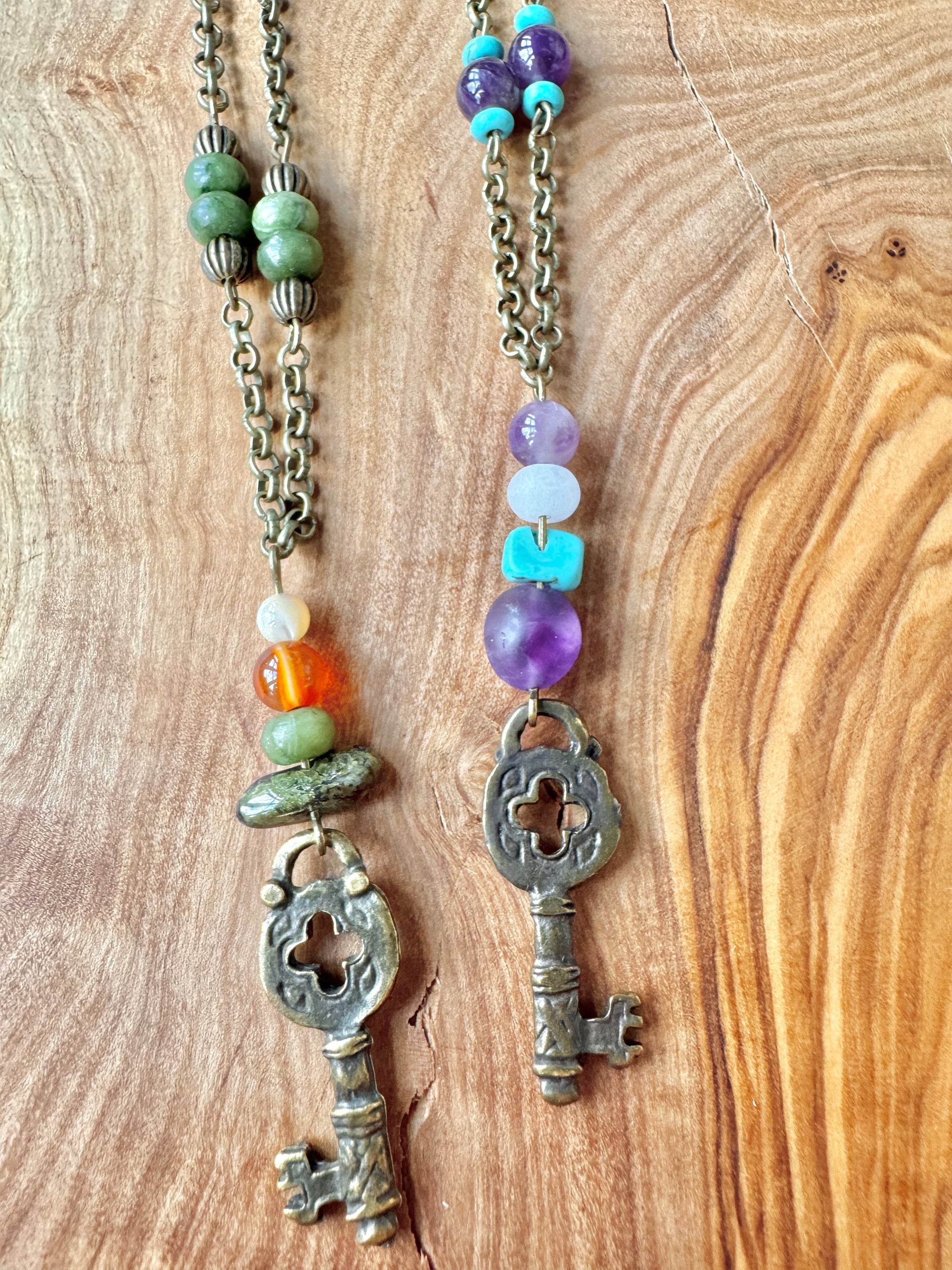 Two key-shaped pendants on chains with colorful beads against a wooden background