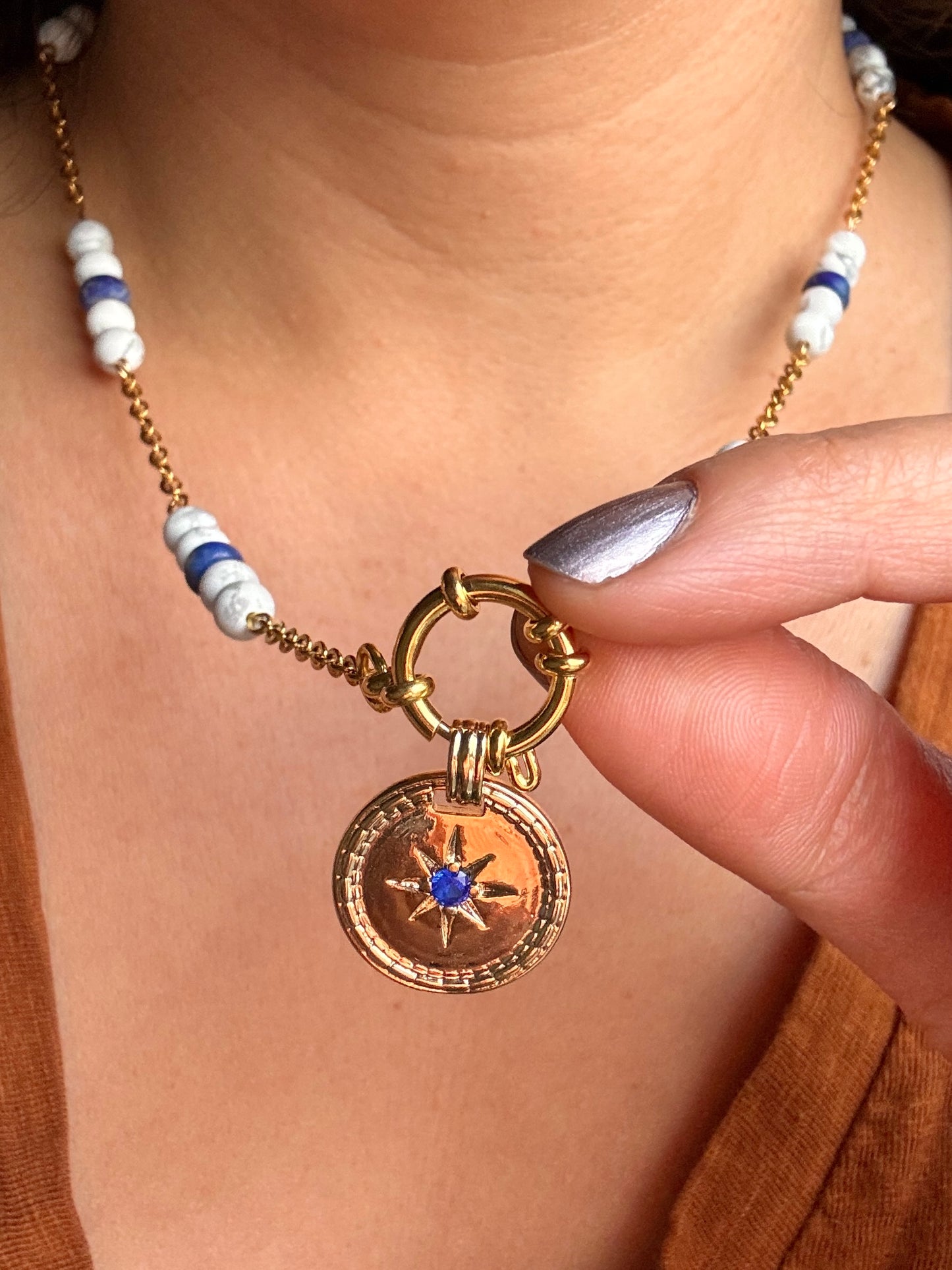 Model holding up blue stone pendant on necklace, close up