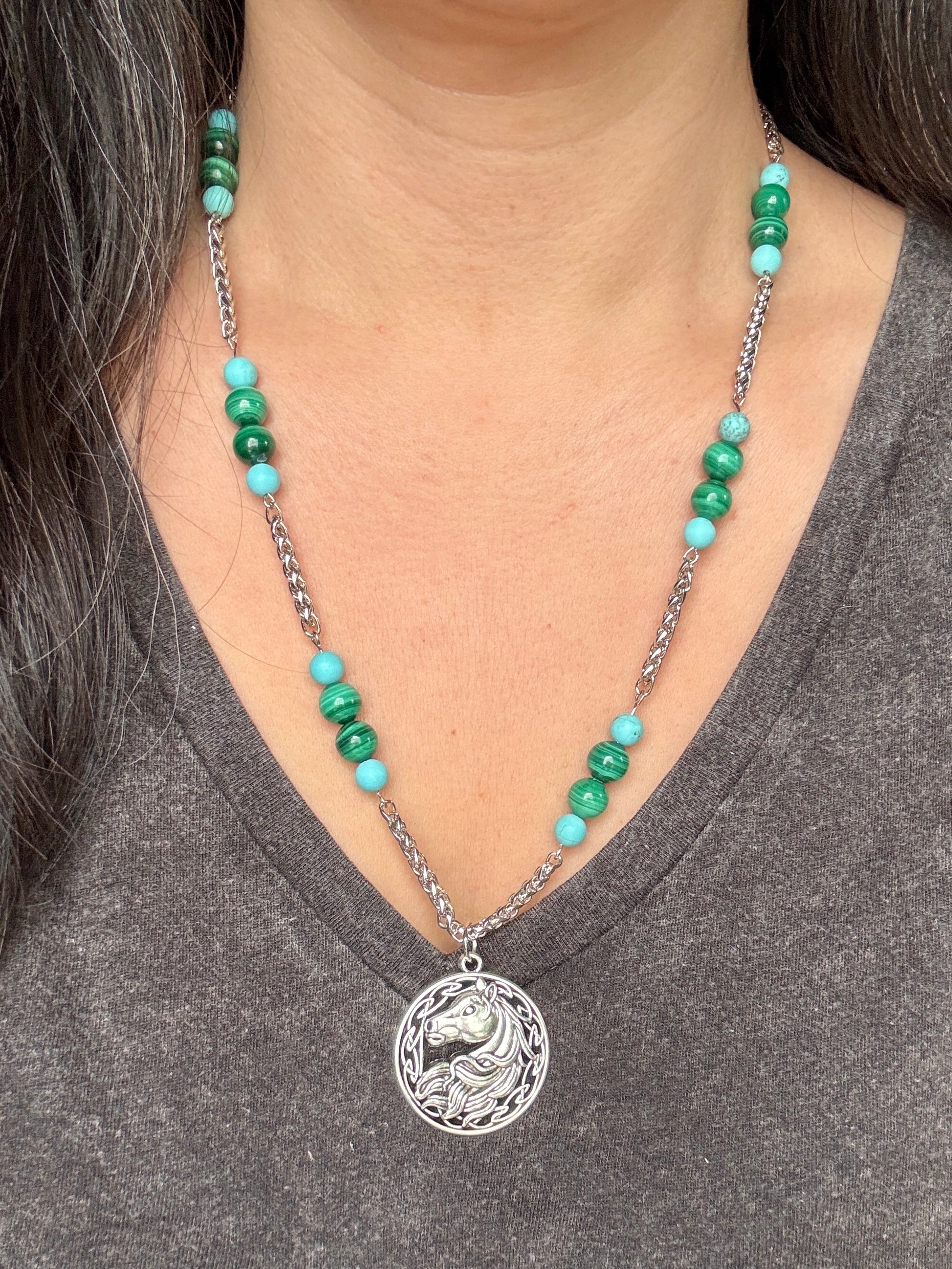 Necklace with green beads and a silver horse pendant worn by a person in a gray shirt.
