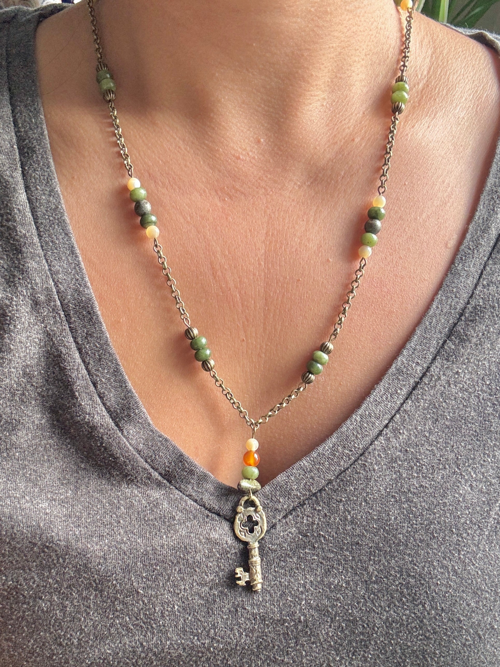 Necklace with a key pendant and beads on a person wearing a gray shirt