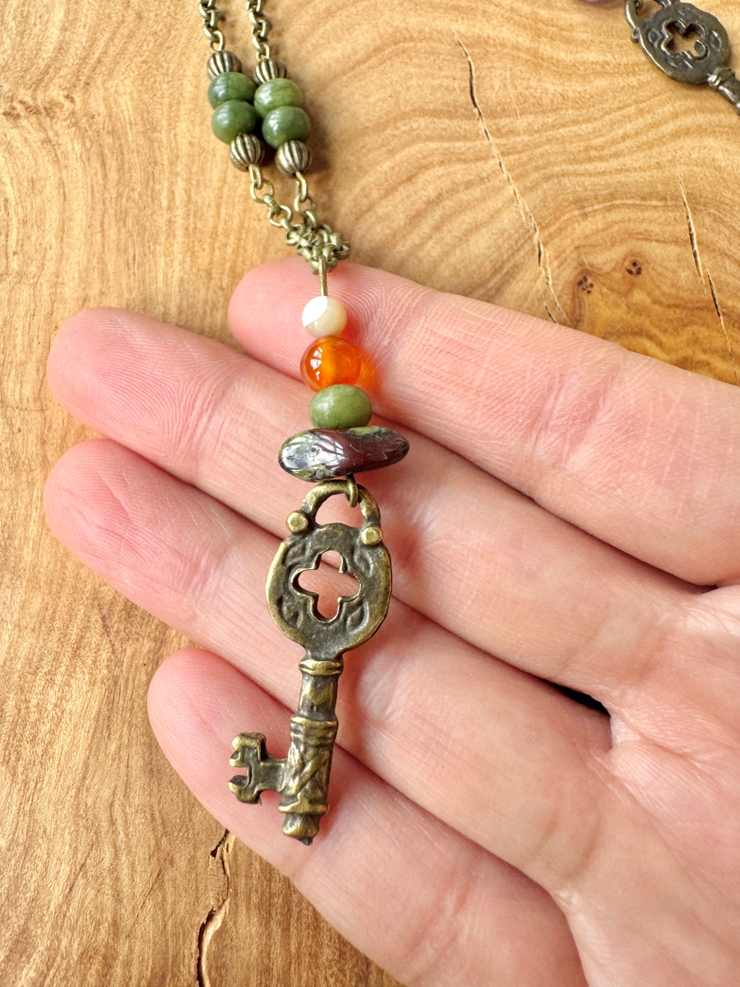 Hand holding a decorative key-shaped pendant with beads on a wooden surface