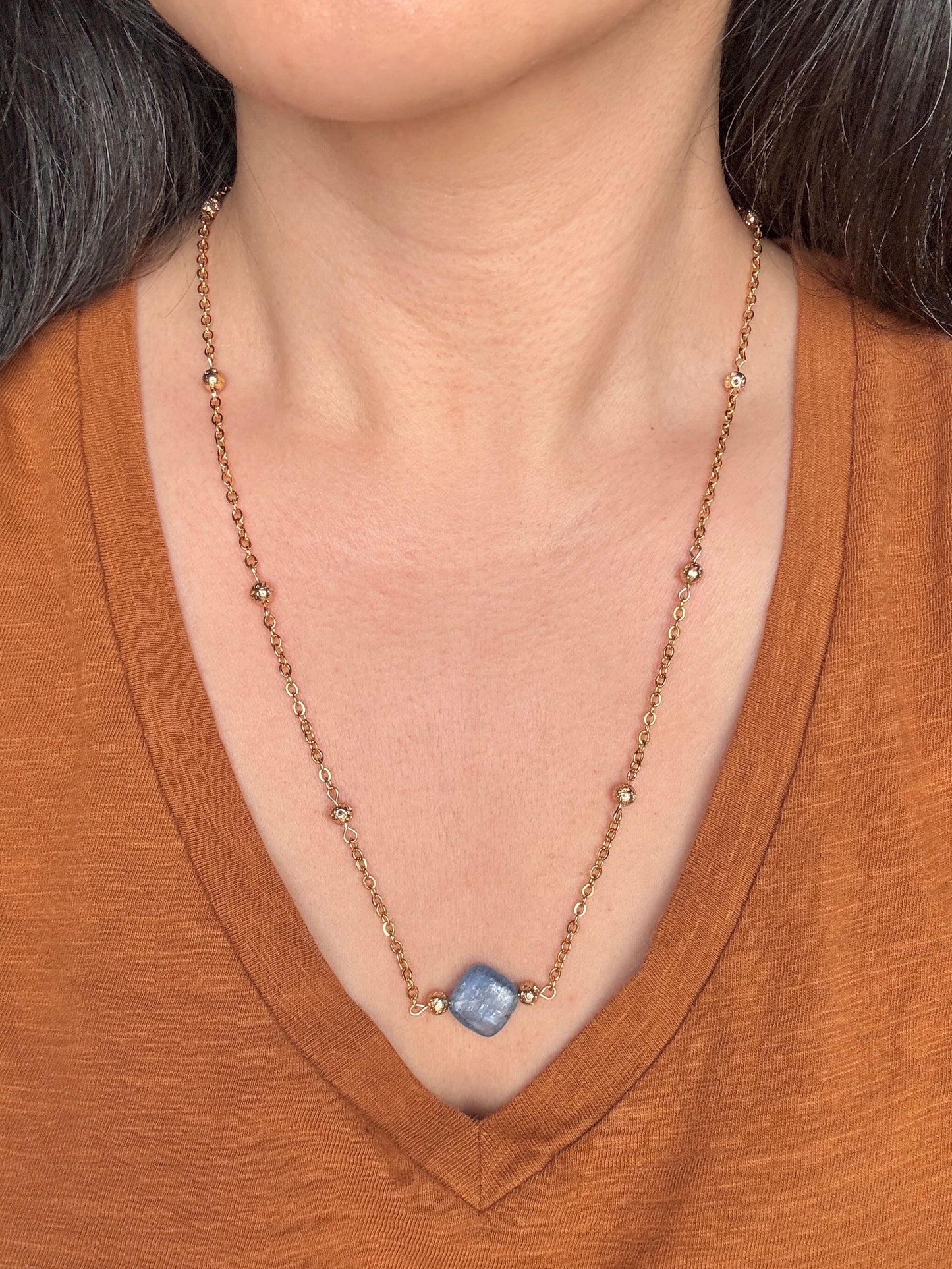 Necklace with a blue gemstone worn by a person in a brown shirt
