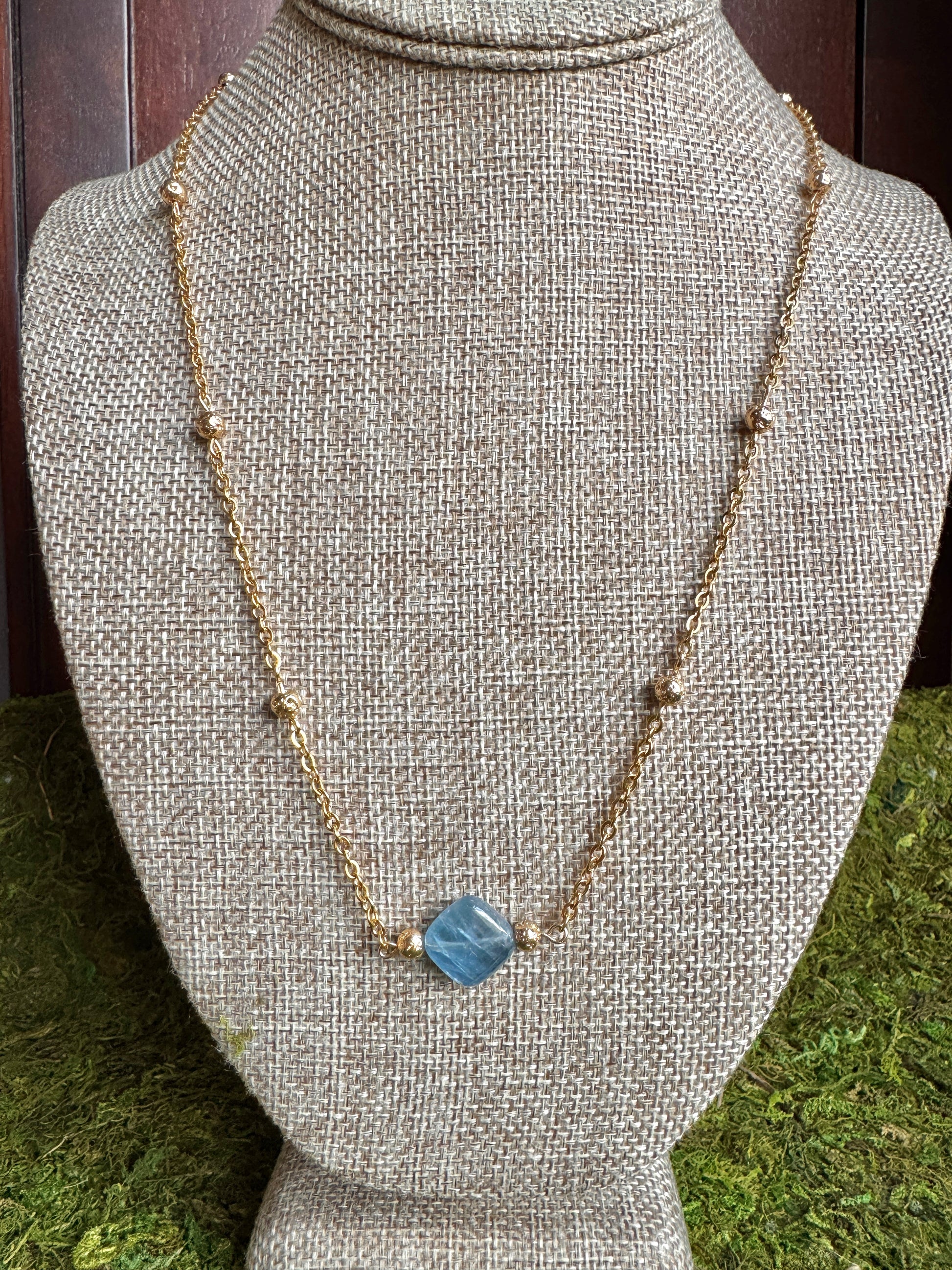 Necklace with a blue pendant on a gray mannequin bust against a green grass background