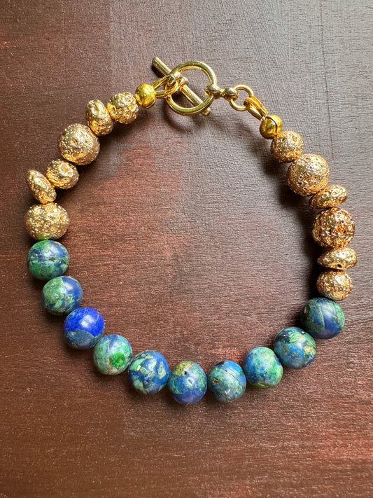 A beaded bracelet with textured gold-colored beads and round blue-green lapis lazuli-style beads, displayed on a dark brown wooden surface.
