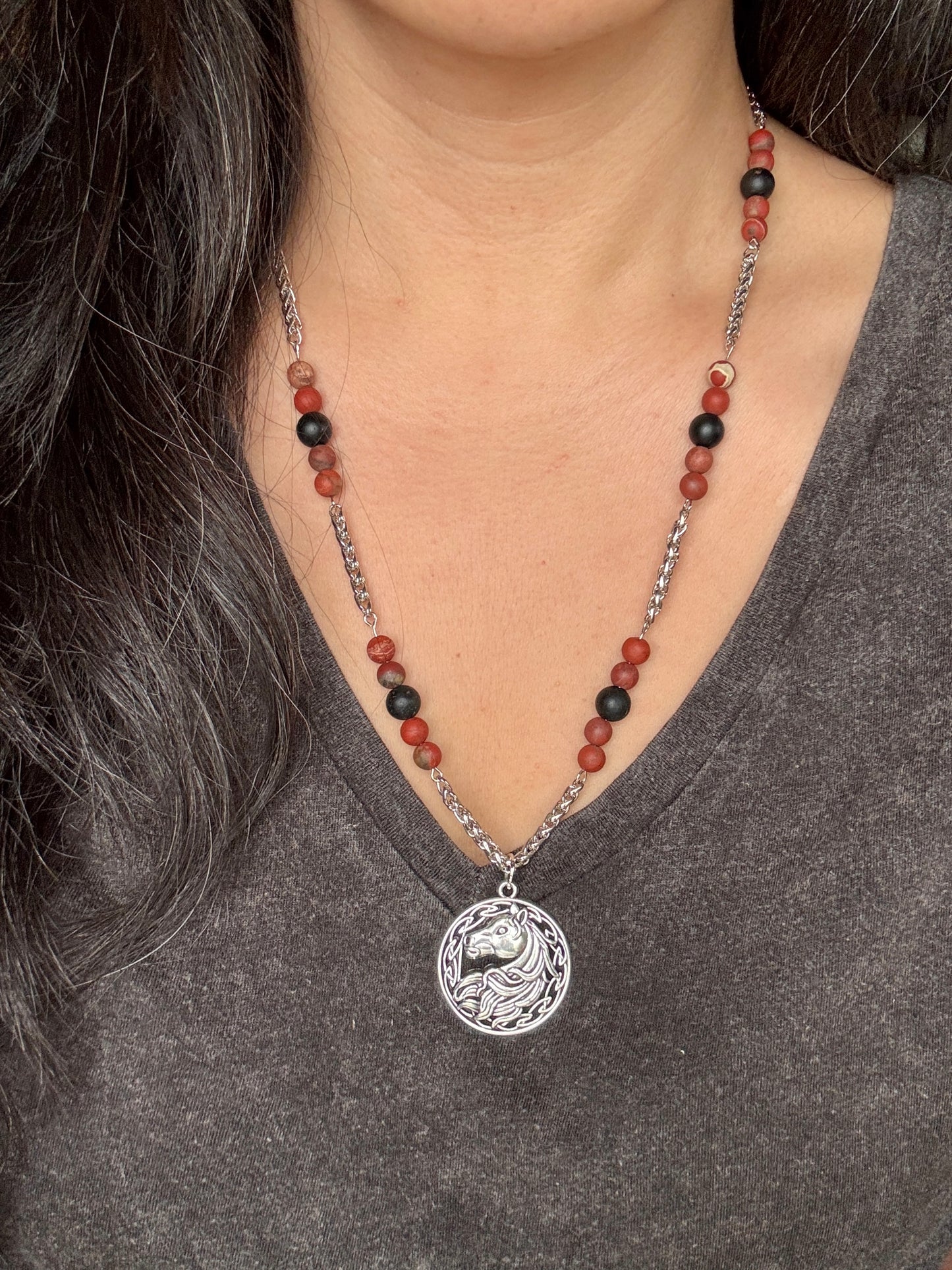 Necklace with a horse pendant worn by a person in a gray shirt
