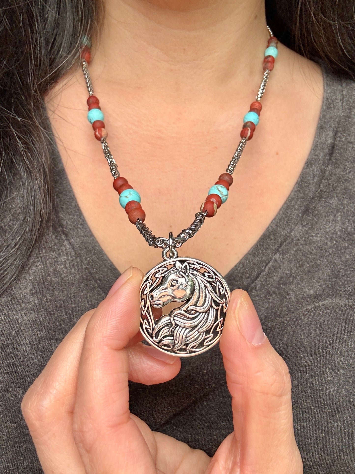 Necklace with a horse pendant held by a person wearing a gray shirt.