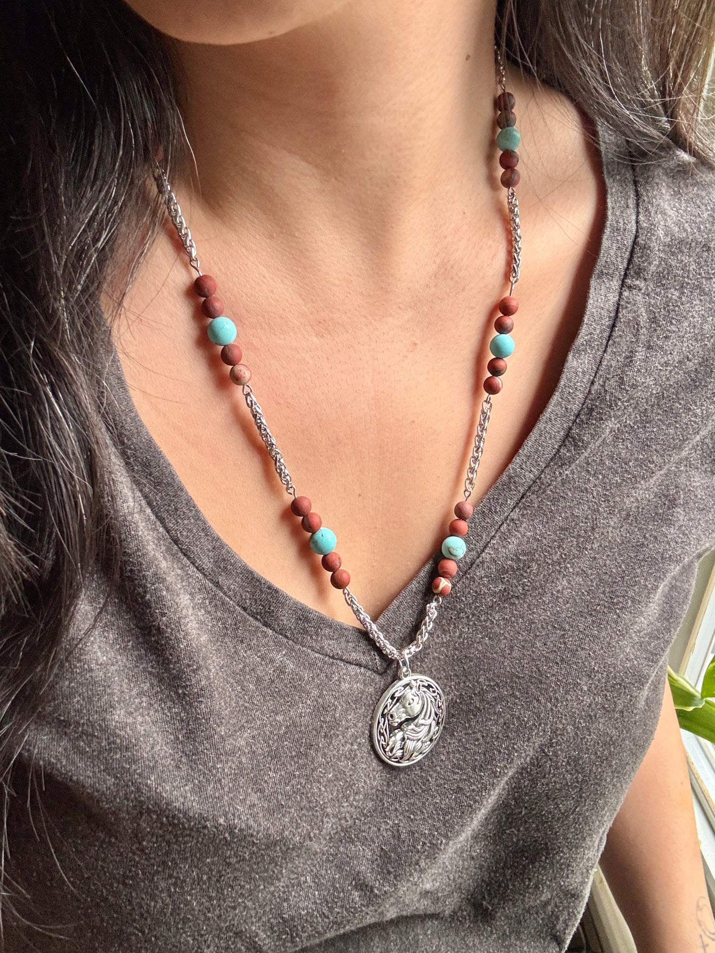 Necklace with a horse pendant worn by a person, featuring turquoise and brown beads.