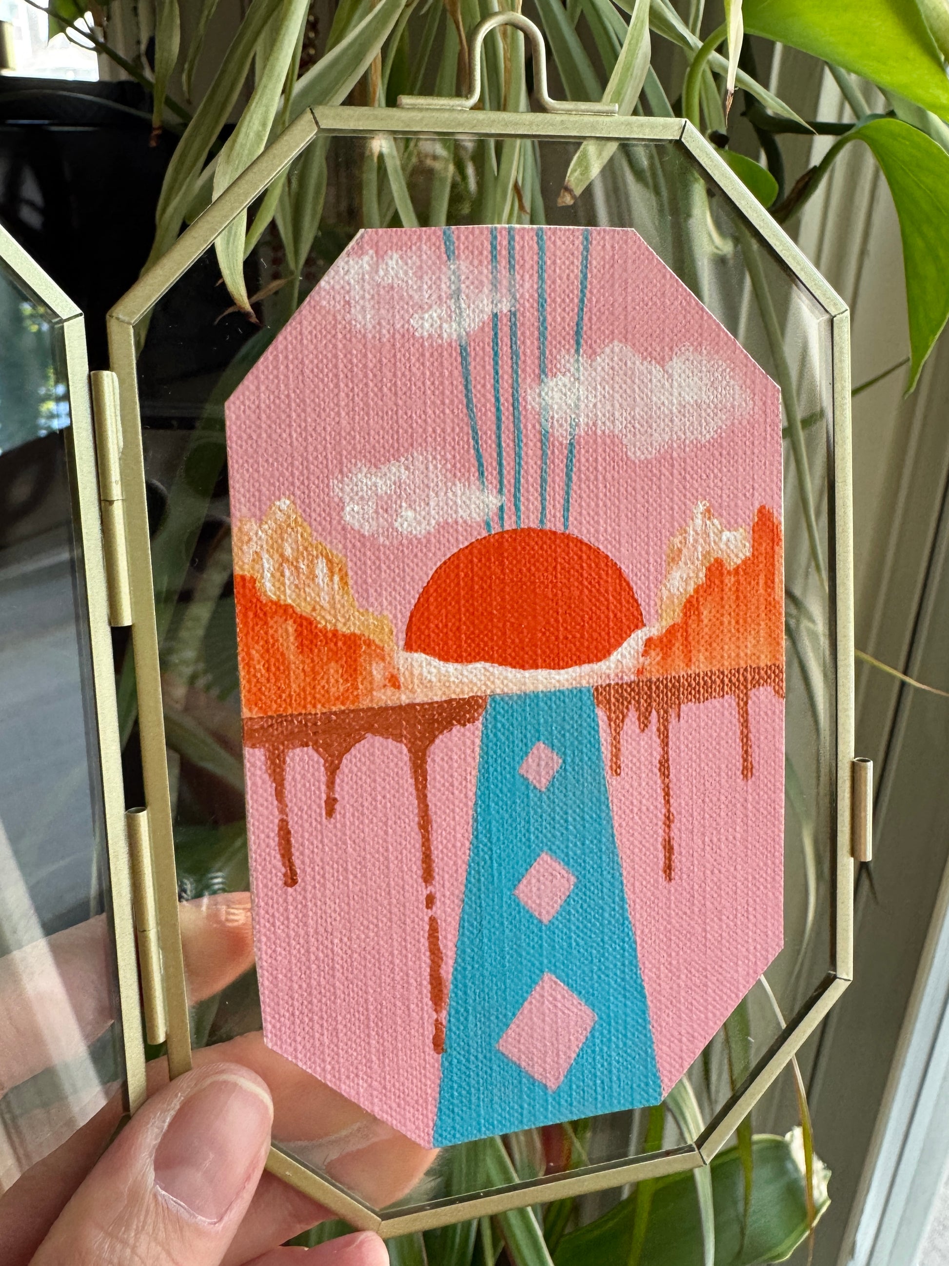 Hand holding up a geometric shape landscape painting against a glass frame 