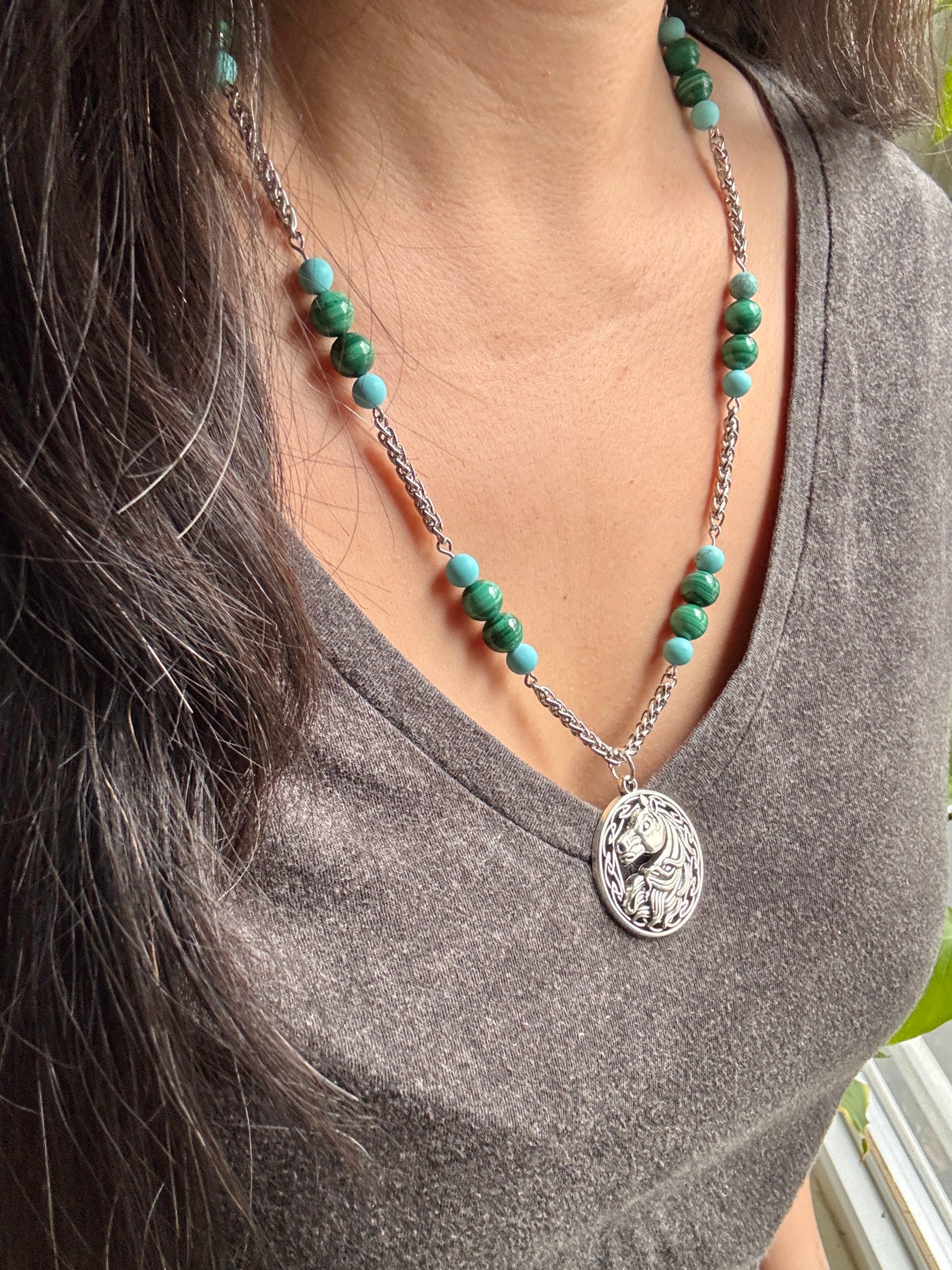 Person wearing a necklace with green beads and a silver pendant