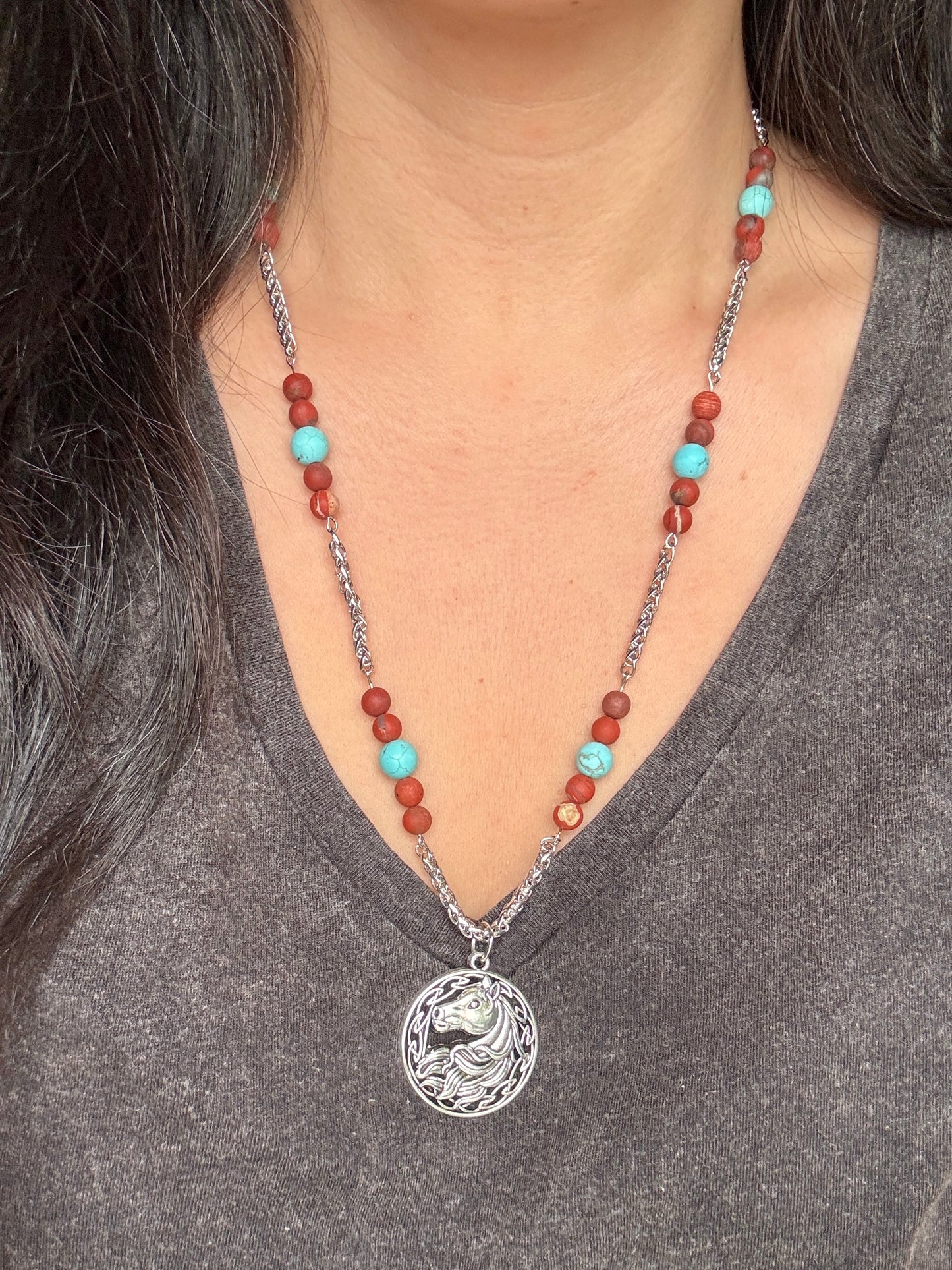 Necklace with a horse pendant and beads worn by a person in a gray shirt