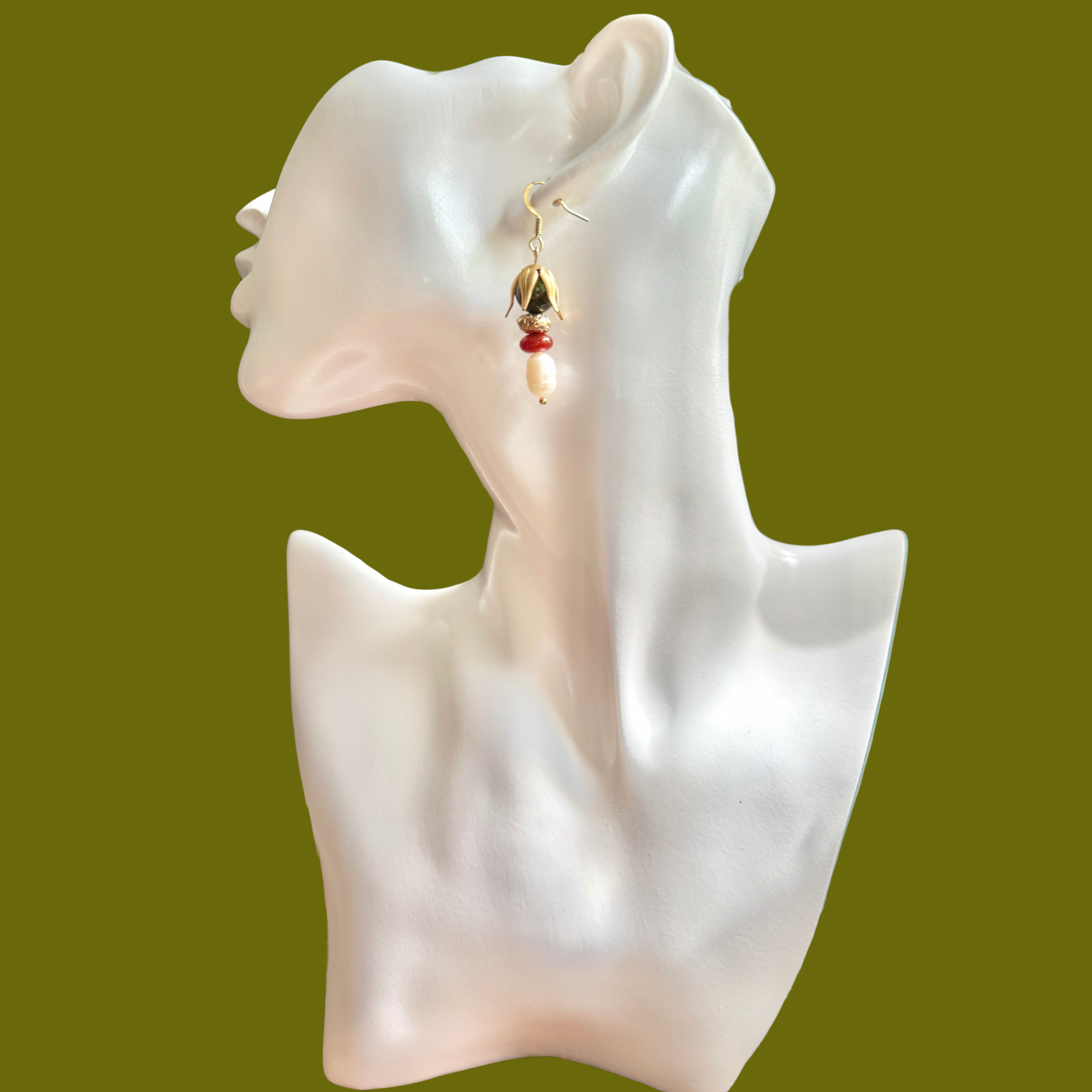 A pair of gold and red beaded dangle earrings displayed on a white female mannequin head against a solid olive green background.