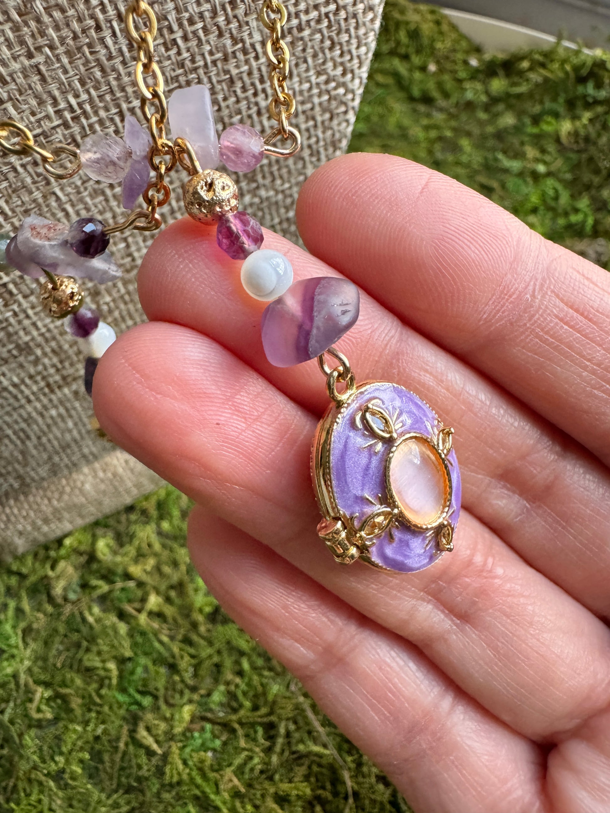 Hand holding a necklace with a purple pendant against a natural background