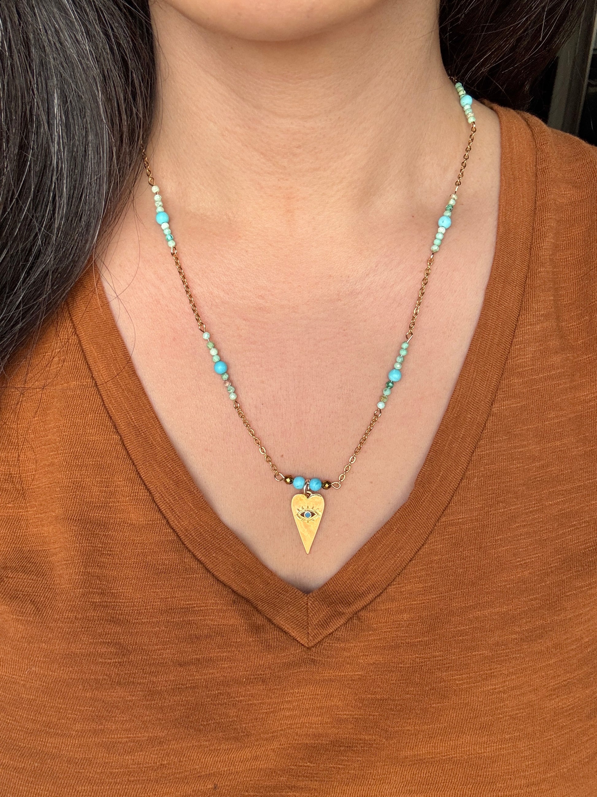 Necklace with a heart-shaped pendant worn by a person in a brown shirt