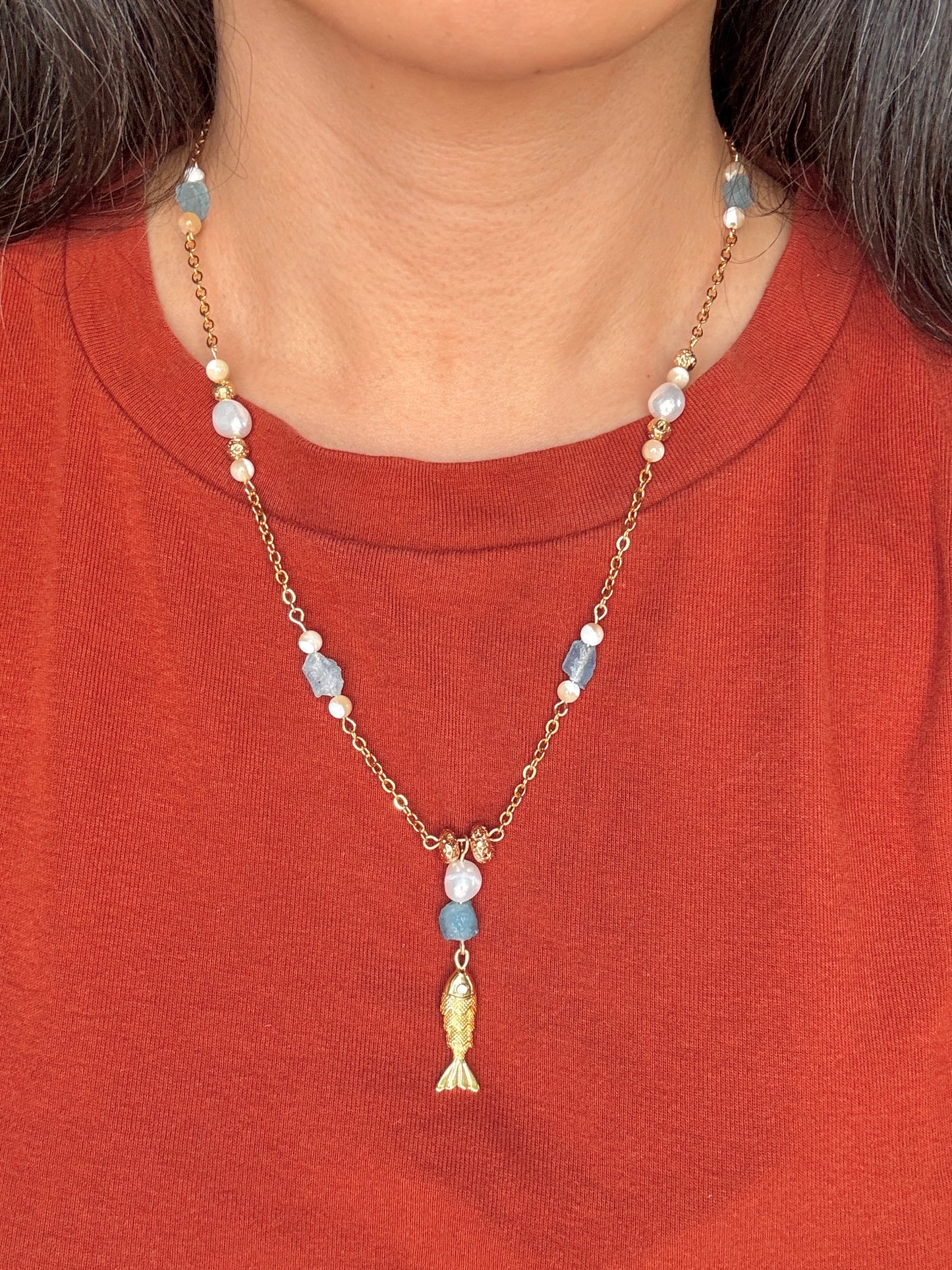 Necklace with a fish pendant worn by a person on an orange shirt