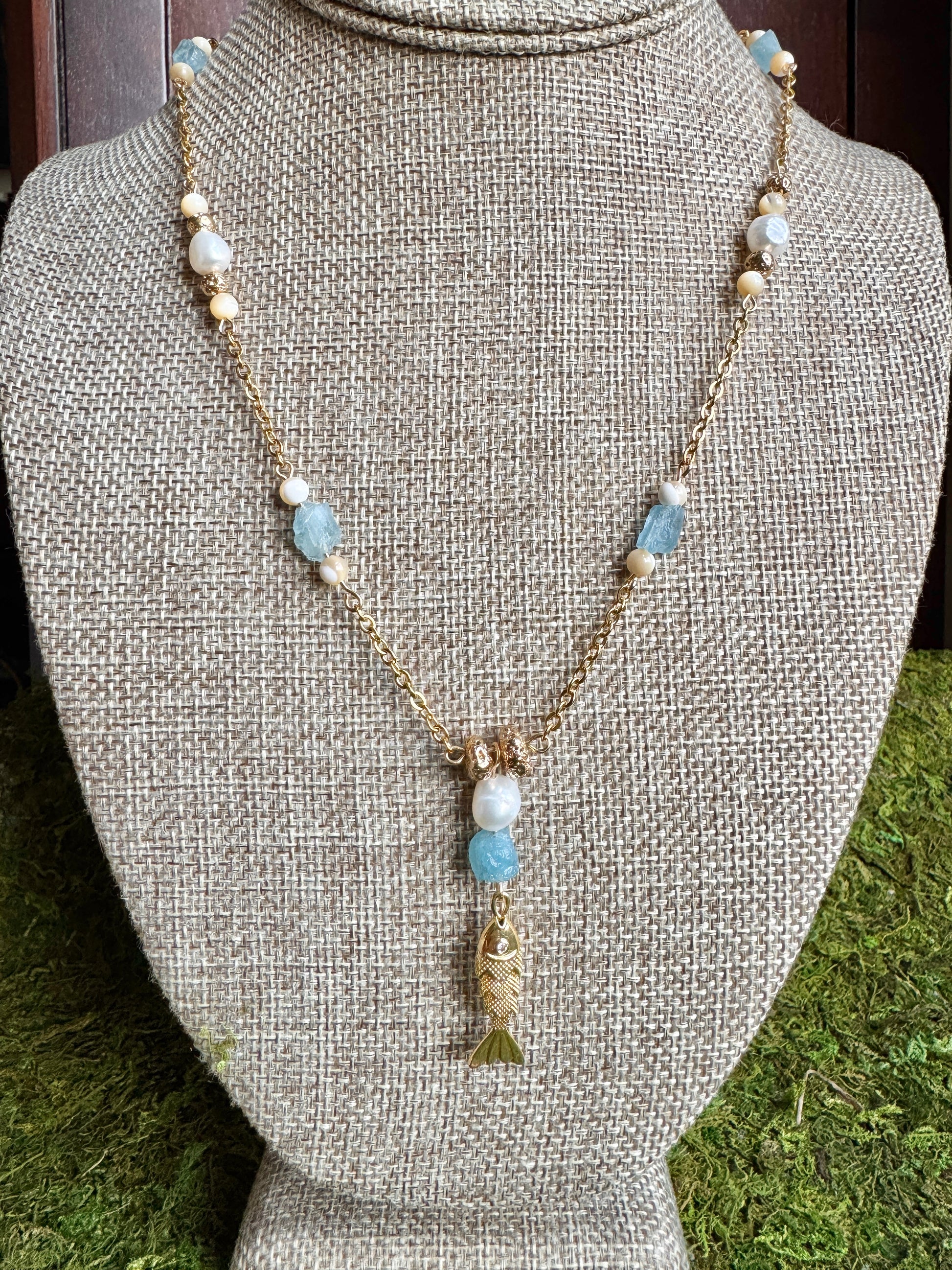Necklace with fish charm and blue and white beads on a mannequin bust.