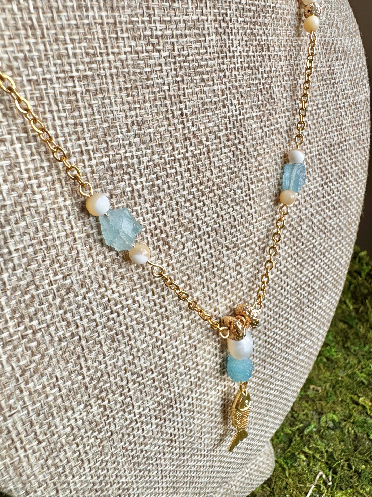Necklace with gold chain and blue and white beads on a textured surface